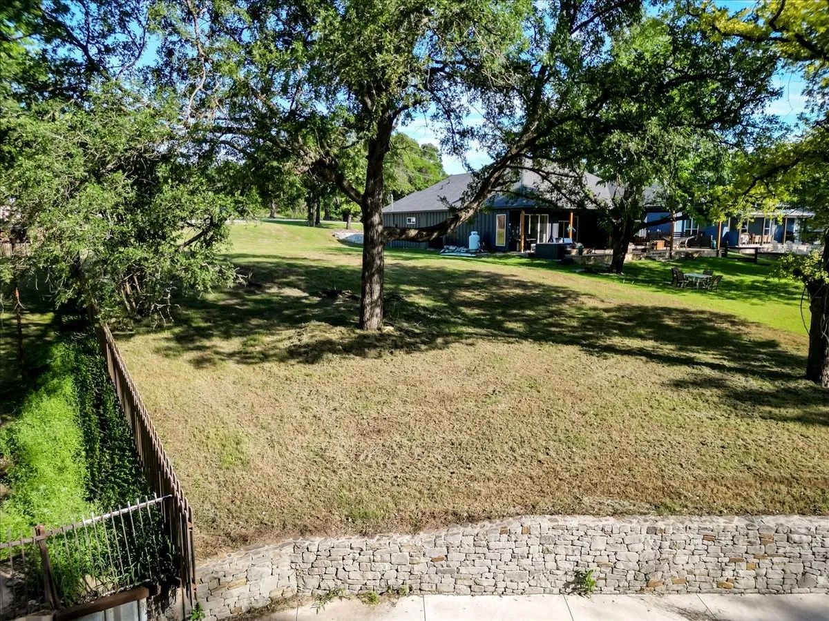 Spacious outdoor area featuring a stone retaining wall, mature trees, and an expansive lawn