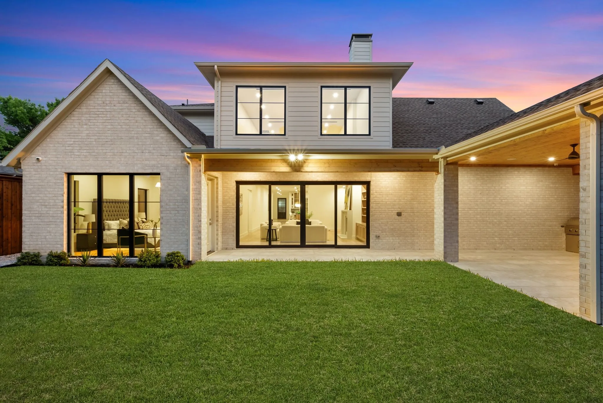 Expansive rear exterior featuring a manicured lawn, a covered patio with recessed lighting and a ceiling fan, and large windows