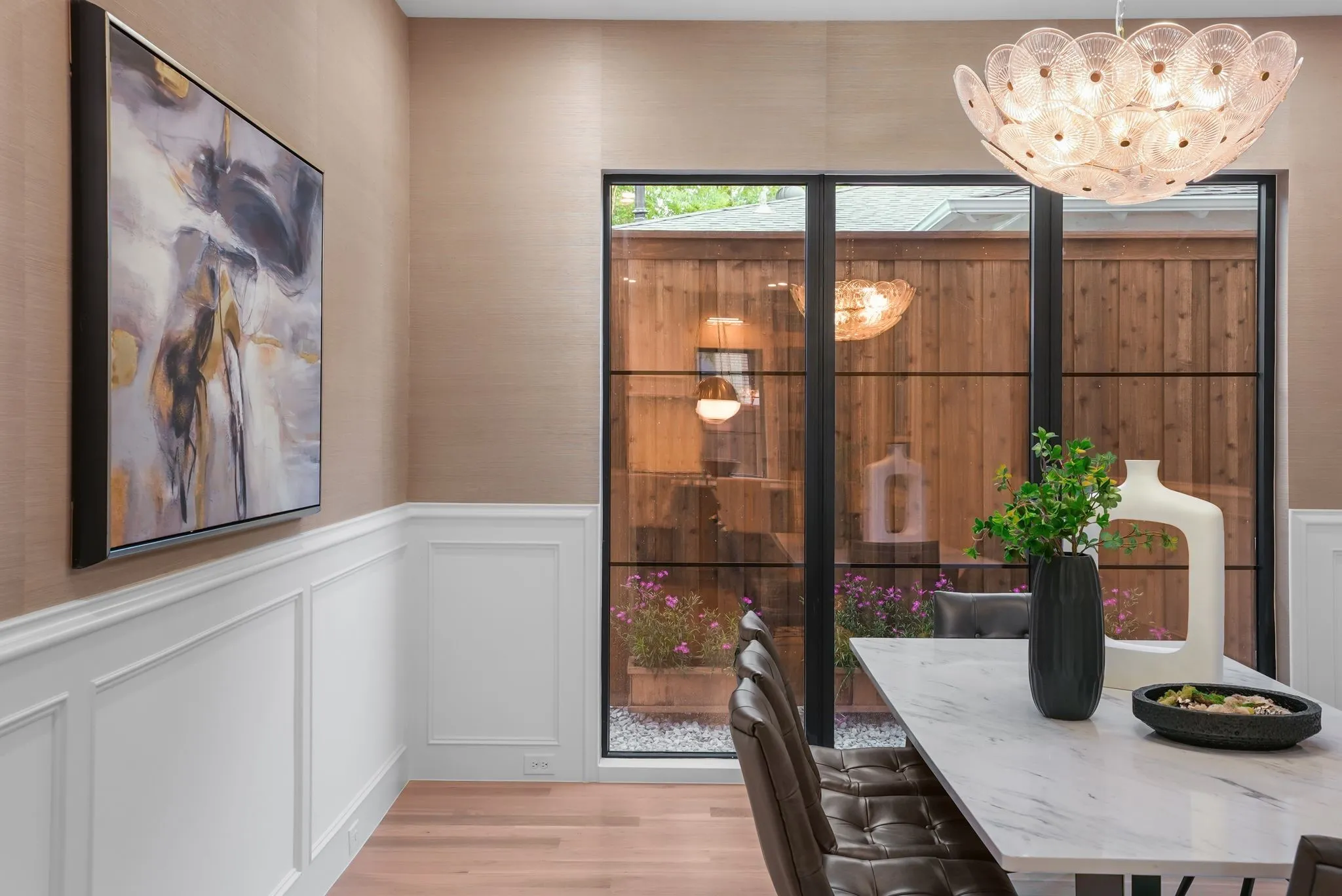Dining area featuring a contemporary chandelier, wainscoting, and large multi-pane windows overlooking a private outdoor space with a wood fence and landscaping