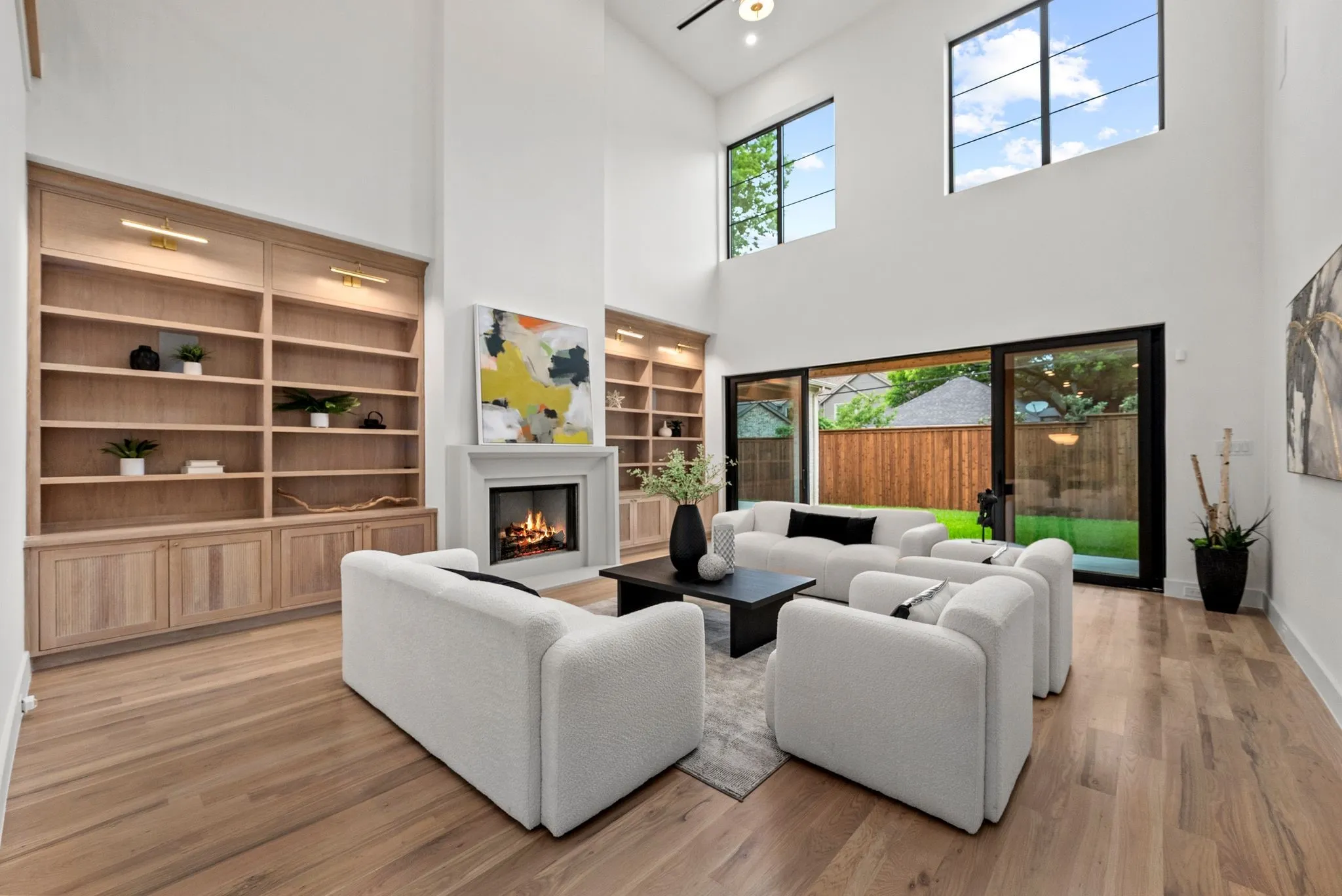 Vaulted living room featuring a fireplace with a mantel, built-in shelving, wood-finish flooring, and expansive sliding glass doors opening to the backyard