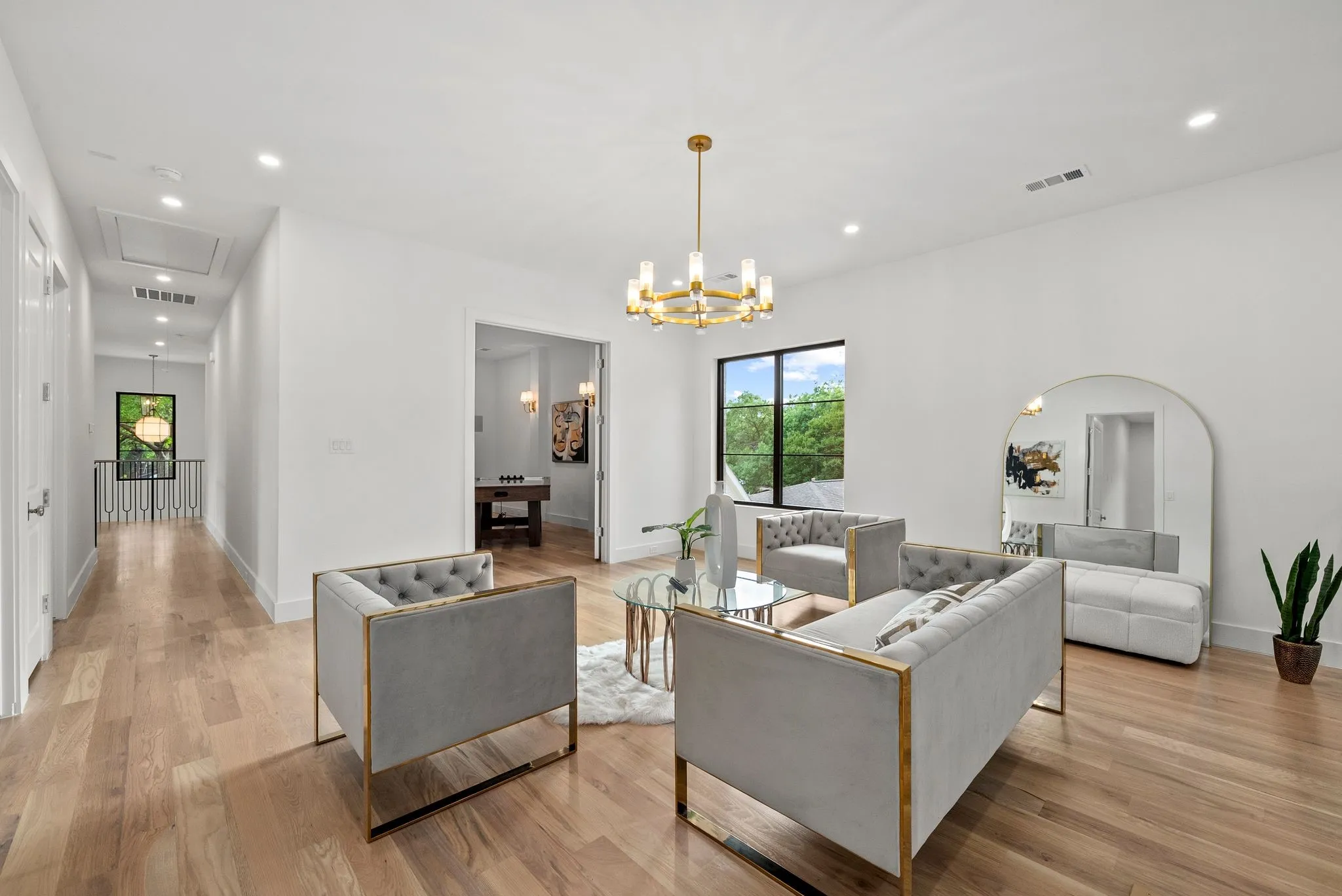 Bright open space featuring hardwood flooring, recessed lighting, a modern chandelier, and a large black-framed window