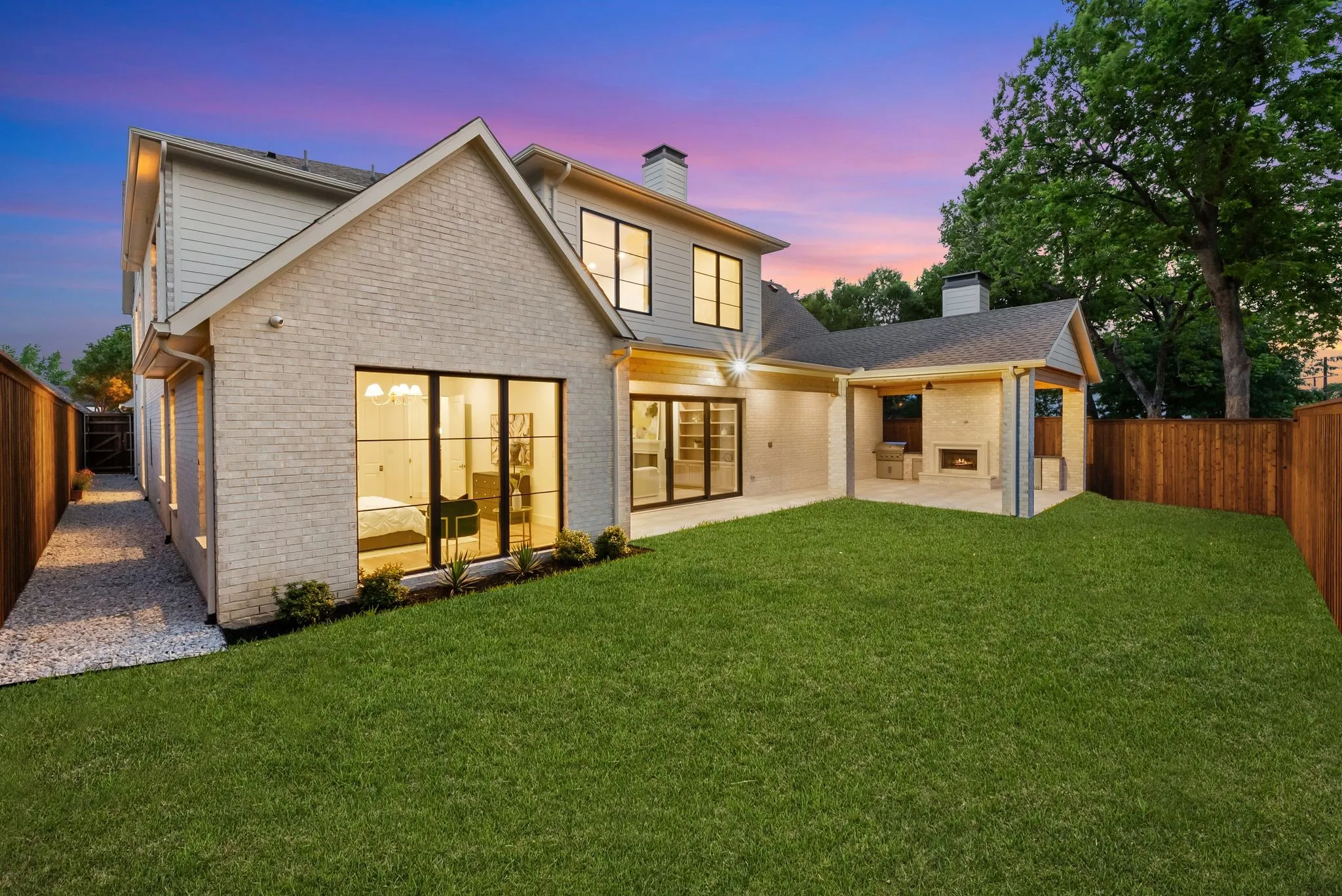 Spacious backyard featuring a manicured lawn, an expansive covered patio with a built-in fireplace, and a side gravel path