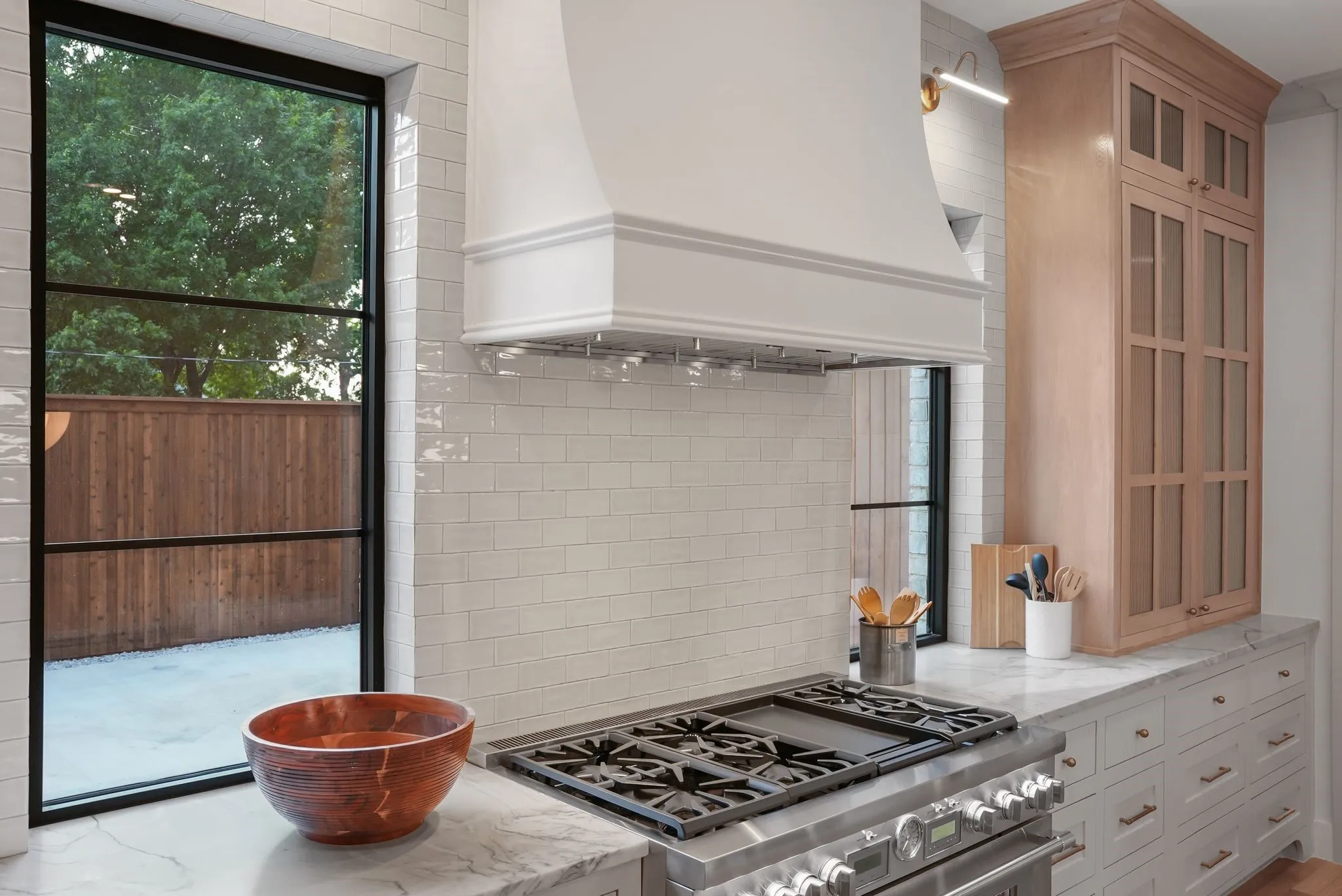 Gourmet kitchen featuring a professional-grade stainless steel range, custom range hood, and light wood cabinetry with glass panel doors