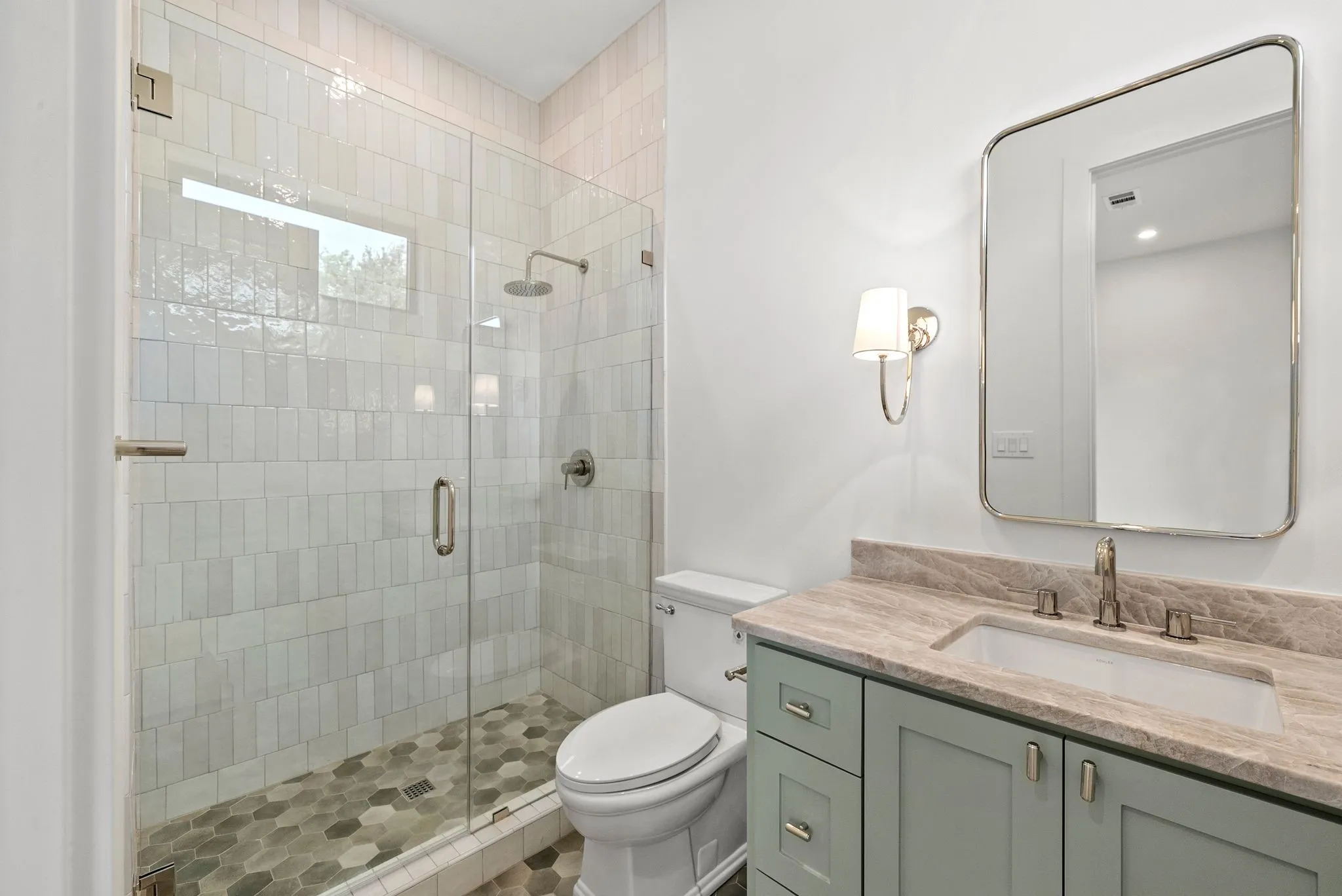 Contemporary bathroom featuring a glass-enclosed shower with vertical subway tile, a hexagonal tile shower floor, a light-toned stone vanity countertop, a rectangular sink, and a framed wall mirror