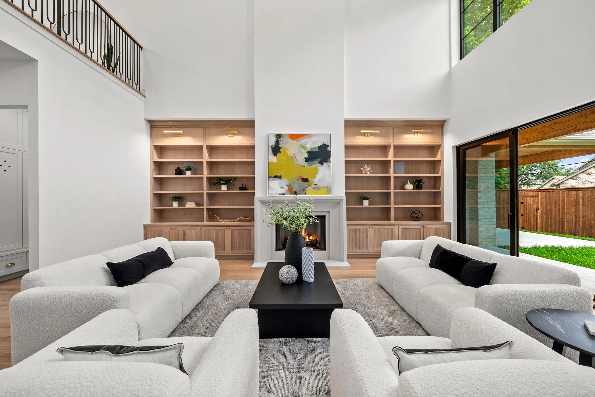 Two-story living area featuring a stone fireplace, built-in shelving with integrated lighting, wood-finish flooring, and a large sliding glass door opening to the exterior
