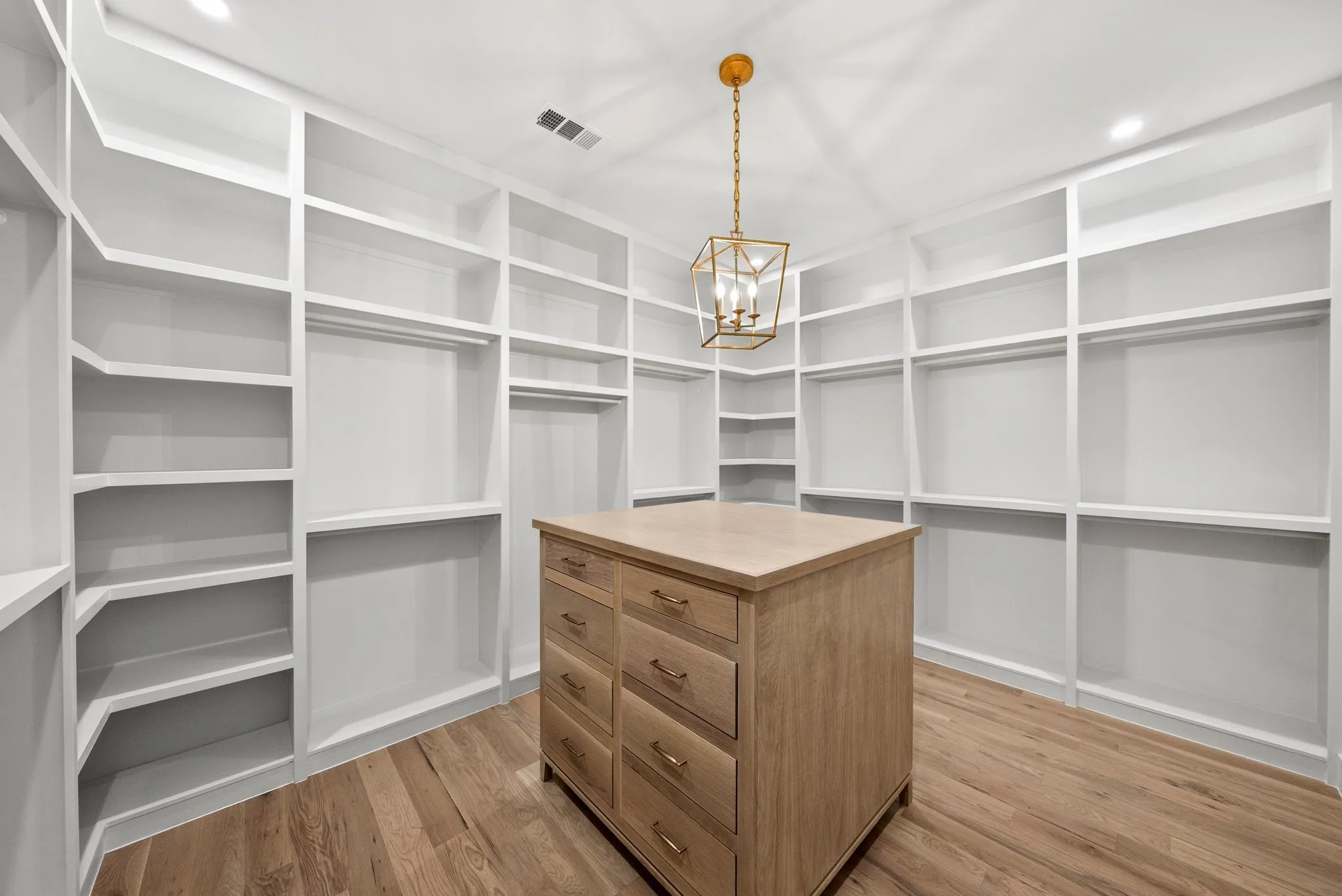Custom closet featuring extensive built-in shelving, hanging rods, and a central wood-finish island with drawers
