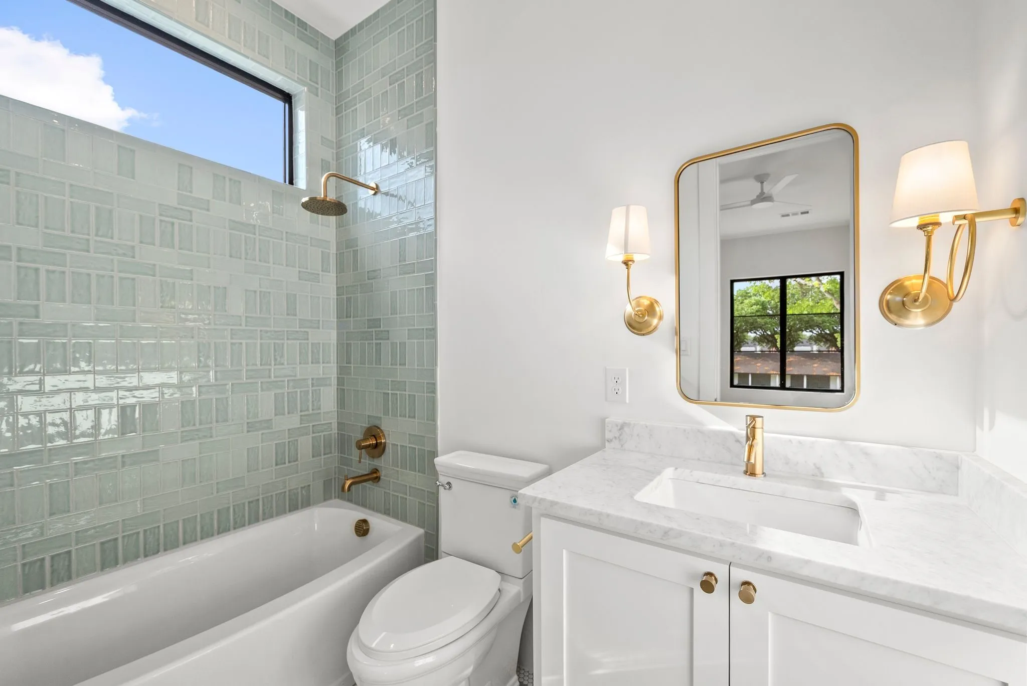 Bathroom featuring a tub/shower combination with a transom window, mosaic tile surround, and gold-finish fixtures