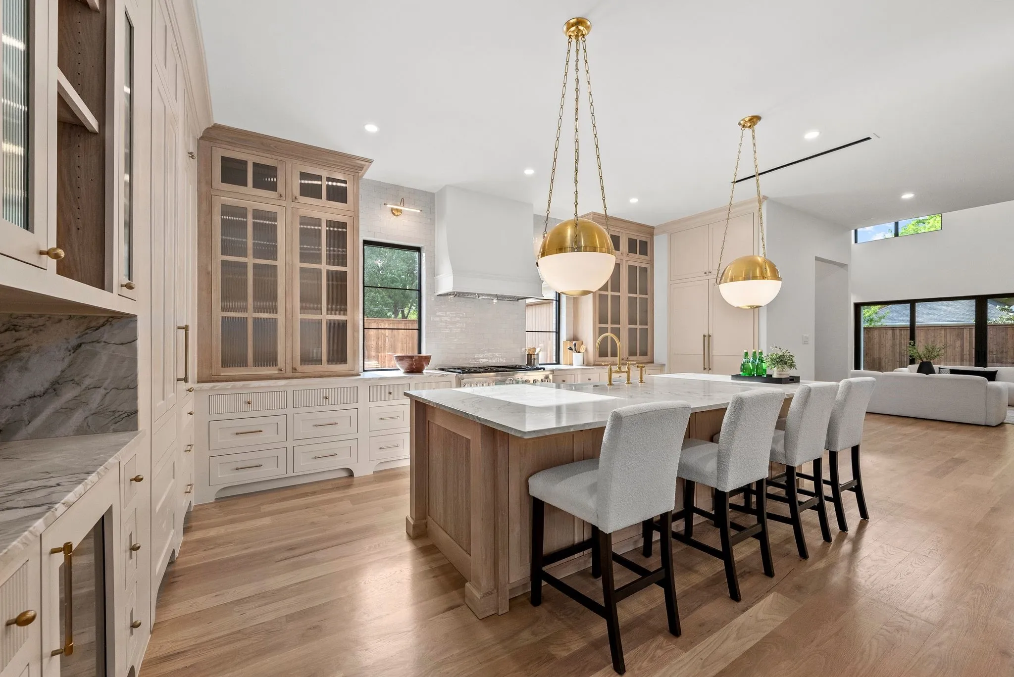 Gourmet kitchen featuring a large central island with seating, natural wood-finish flooring, custom cabinetry with glass fronts, and two statement pendant light fixtures