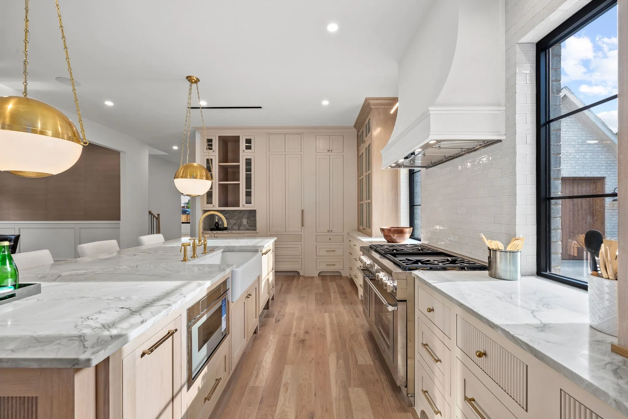 Gourmet kitchen featuring a large island with integrated microwave, farmhouse sink, professional-grade range, and custom cabinetry with gold-tone hardware