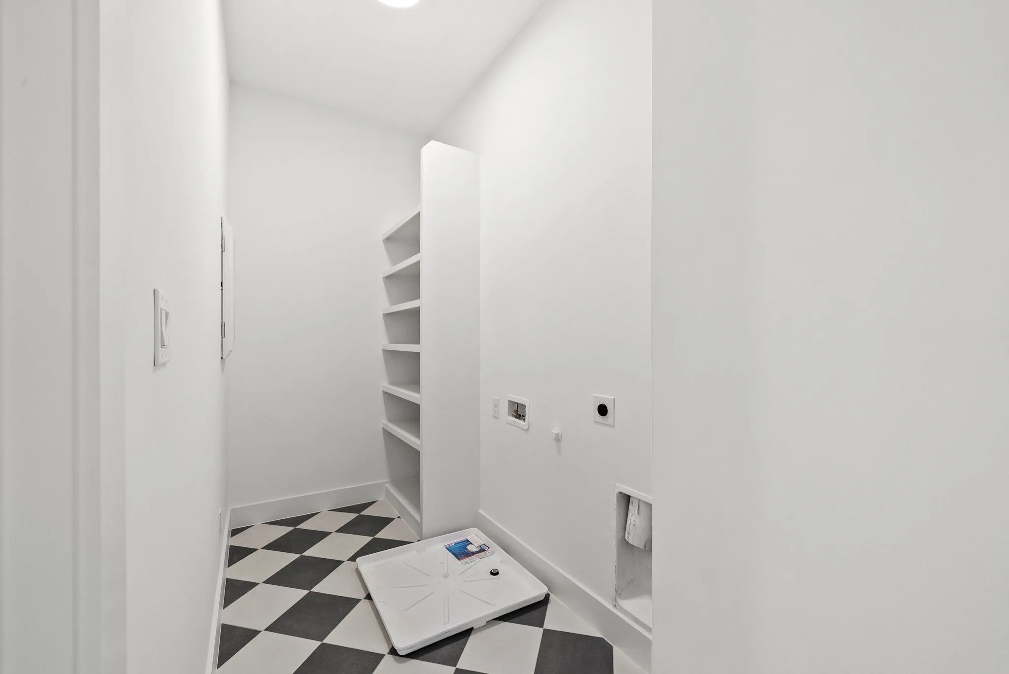 Laundry area featuring a black and white checkerboard tile floor, built-in shelving, and white baseboards