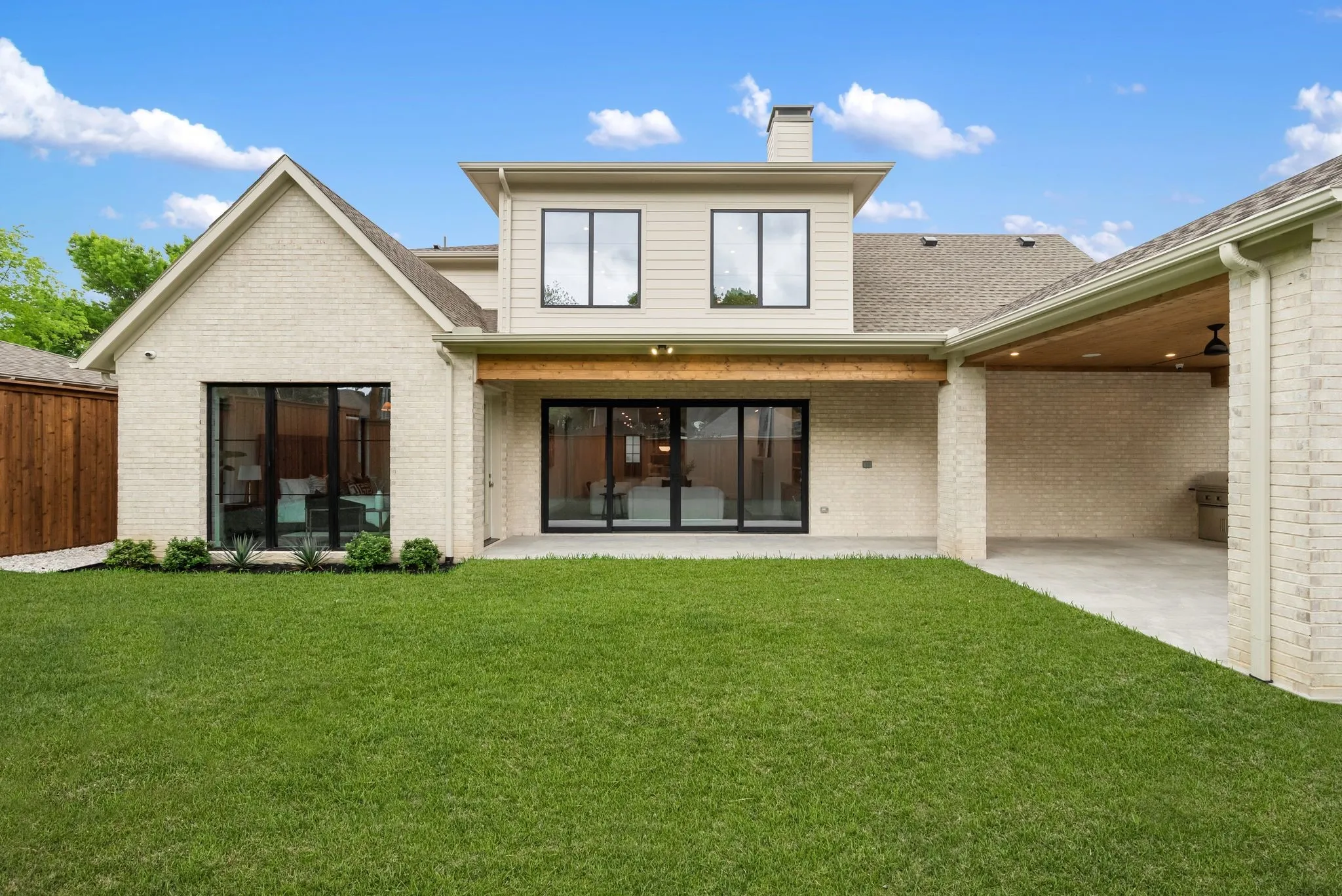 Expansive backyard featuring a manicured lawn, brick and siding exterior, large sliding glass doors, a covered patio with a wood-paneled ceiling, and recessed lighting
