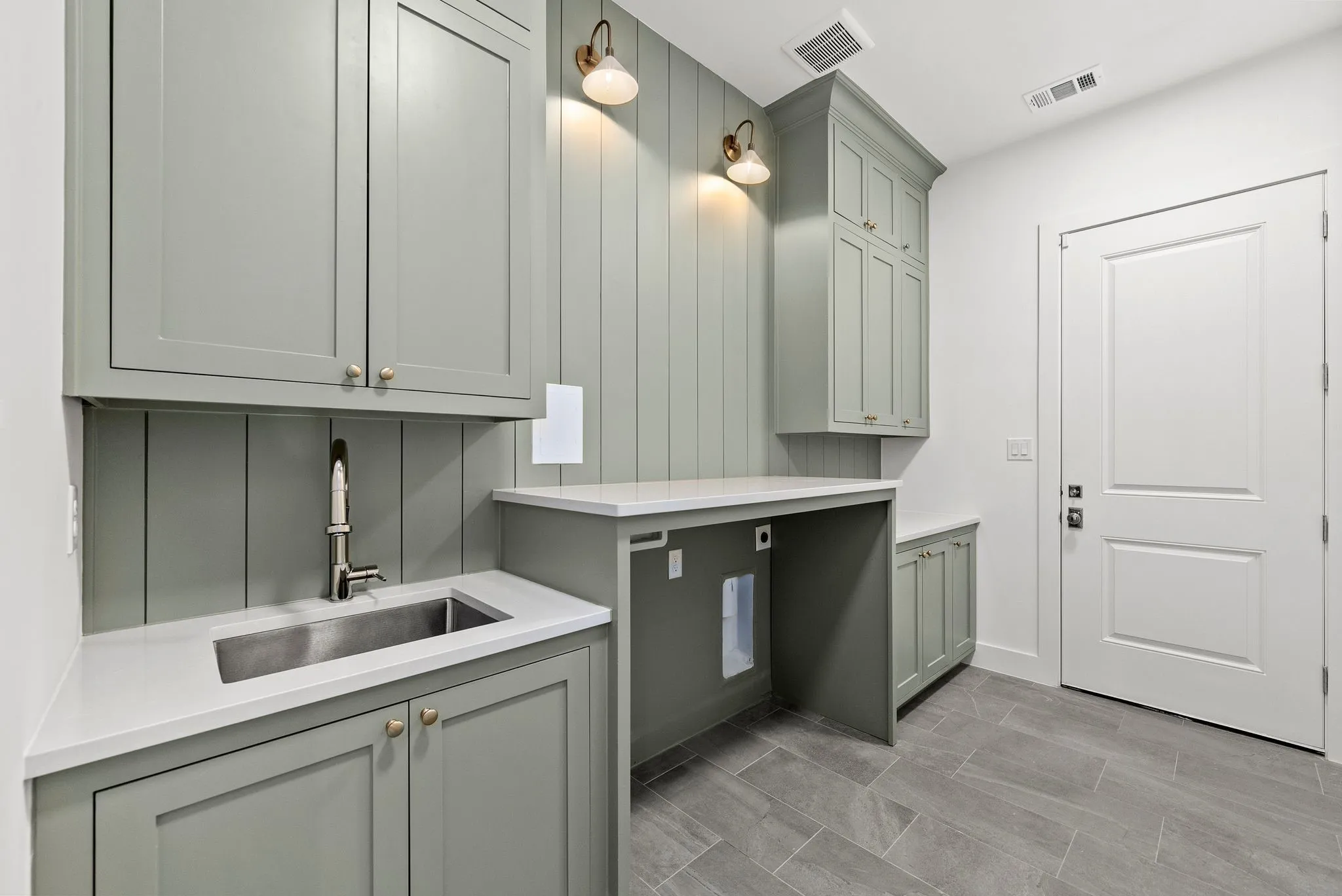 Utility room featuring shaker-style cabinetry, a stainless steel sink with a gooseneck faucet, light-toned countertops, and plank-style tile flooring