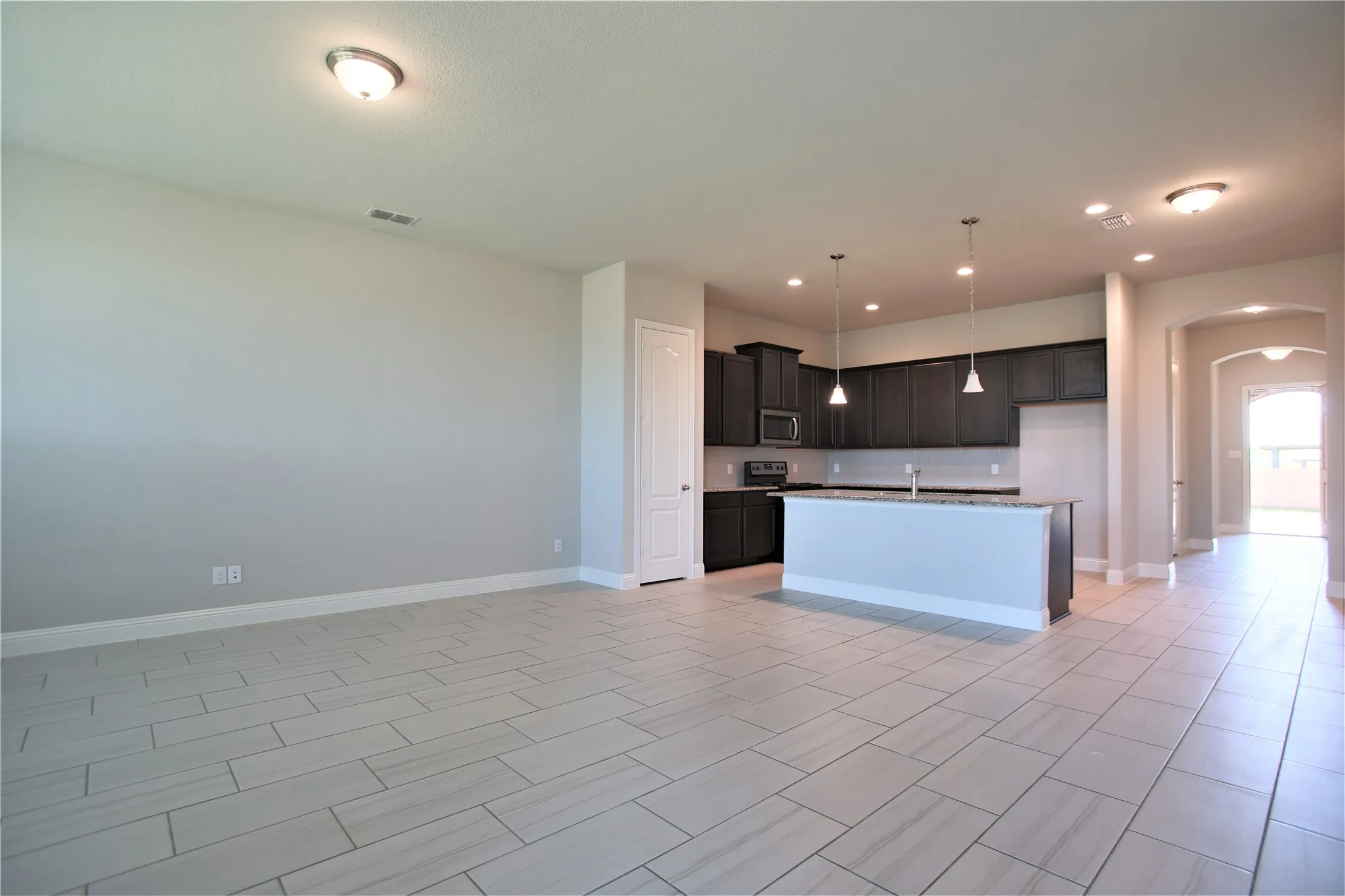 Open-concept living space featuring wood-finish tile flooring, recessed lighting, and a kitchen island with pendant lights