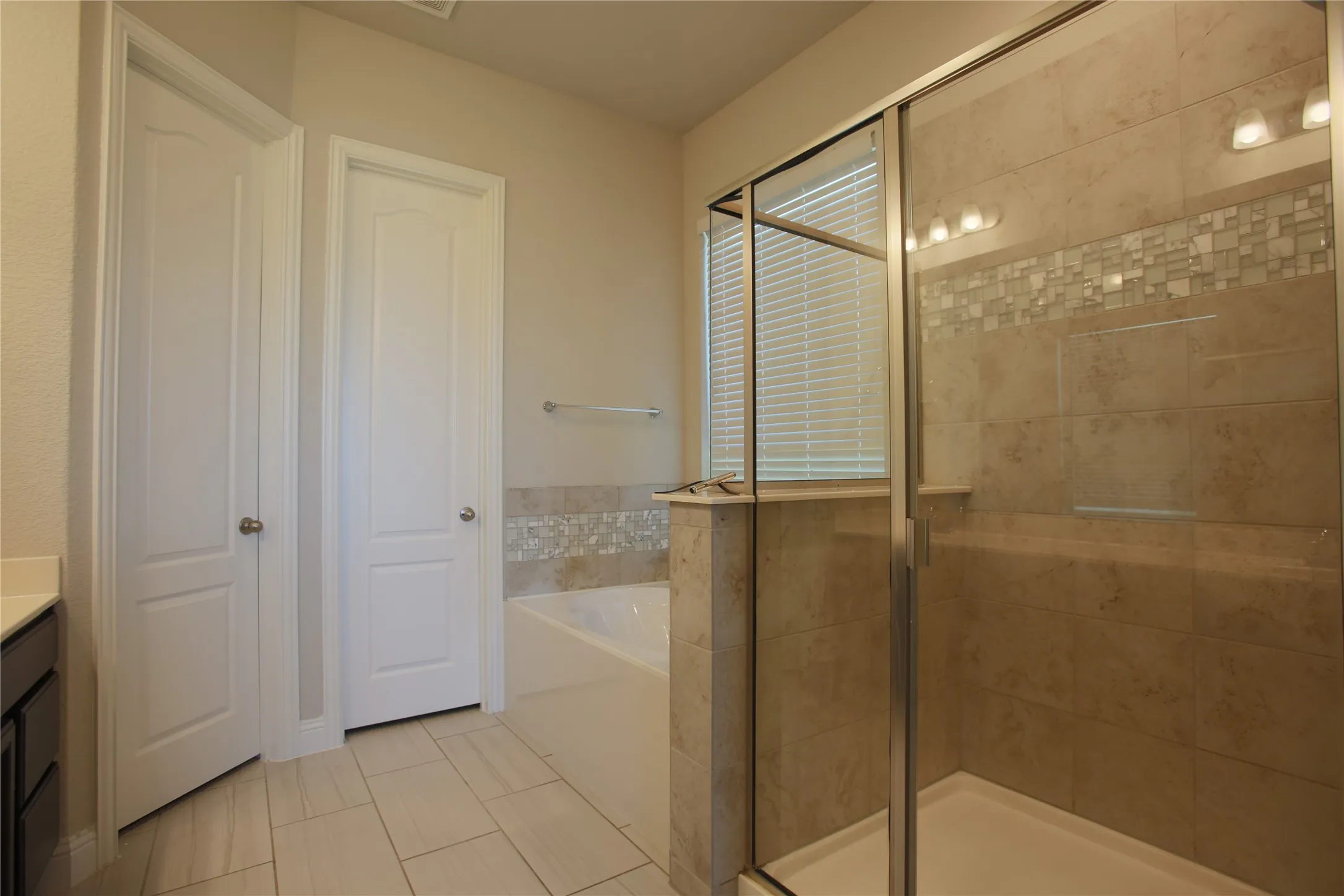 Glass-enclosed shower featuring subway tile with a decorative mosaic band and a built-in shelf