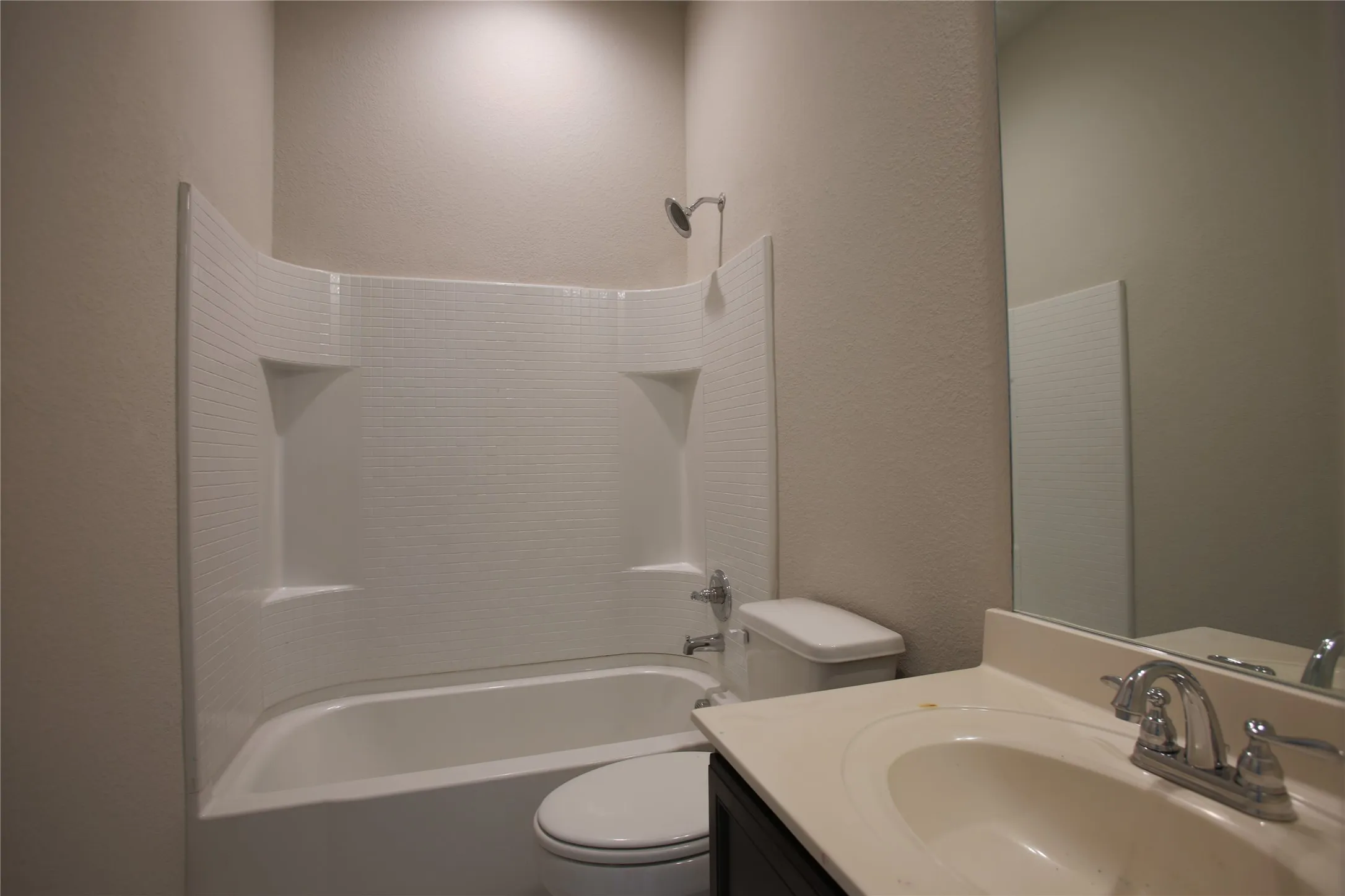 Full bathroom featuring a shower-tub combination with integrated shelving, a white toilet, and a vanity with an integrated sink and chrome faucet