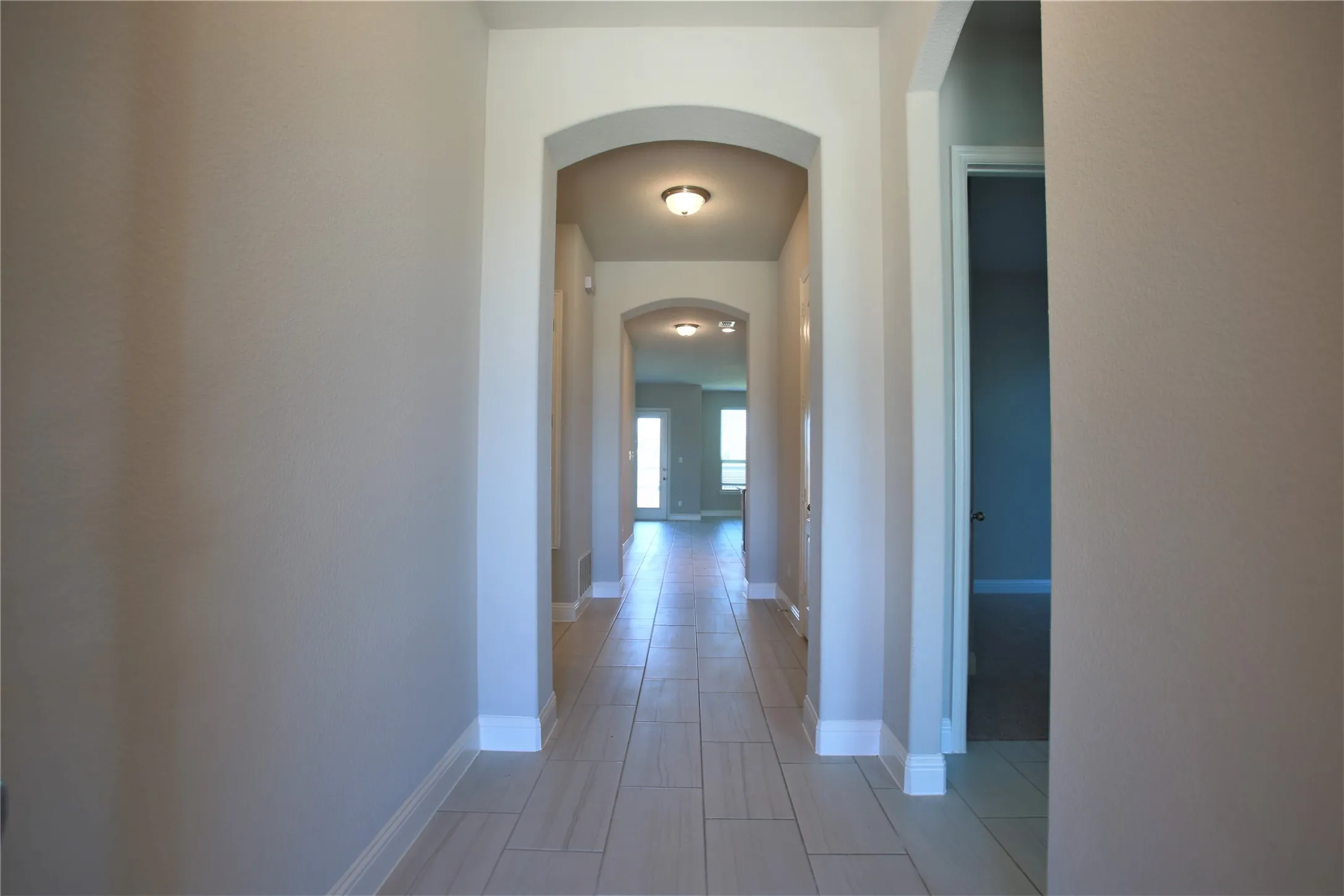 Hallway featuring light-toned flooring, arched doorways, neutral paint, recessed lighting, and white baseboards