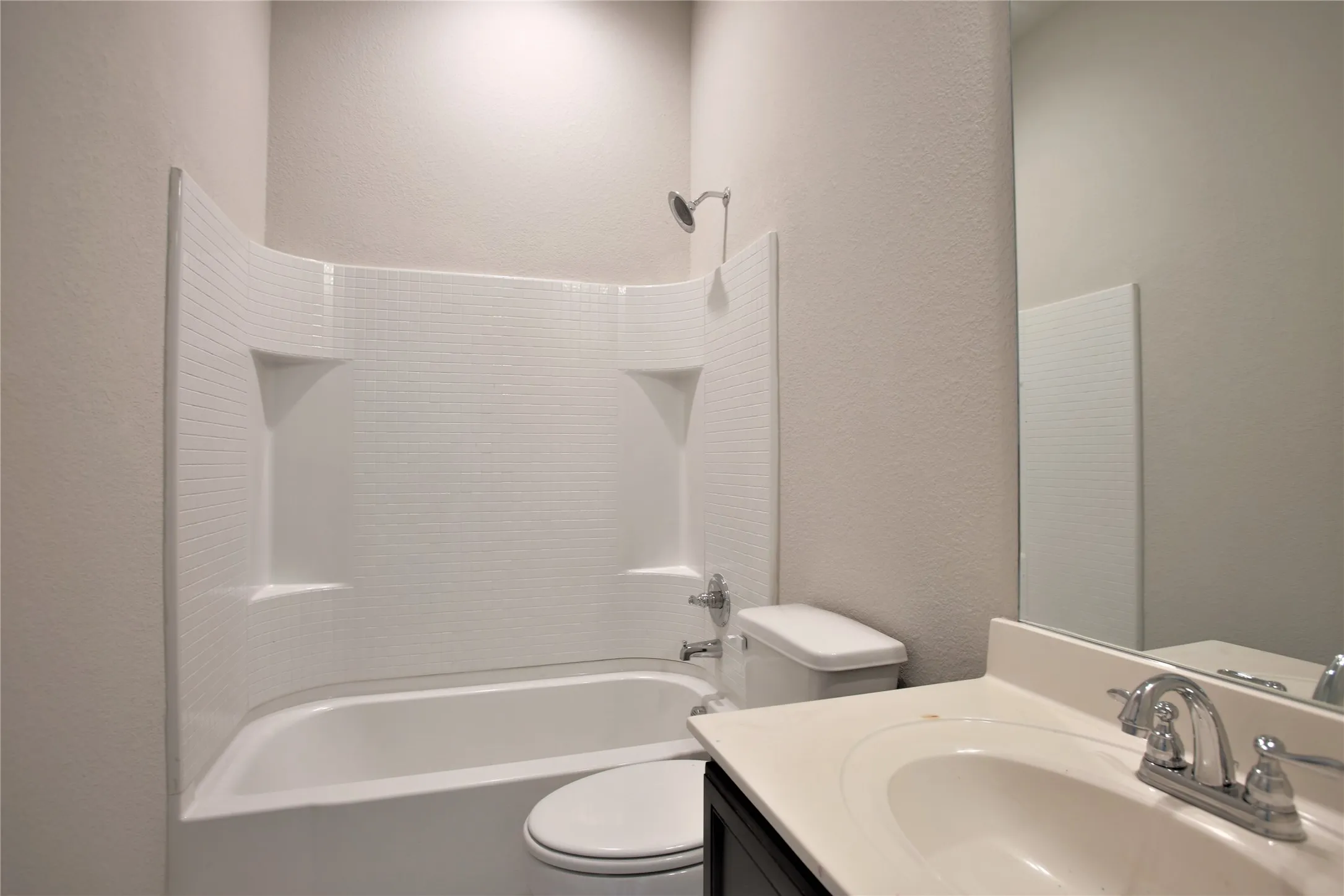 Bathroom featuring a white tub/shower combination with built-in shelving, a toilet, a vanity with a white countertop, and a chrome faucet