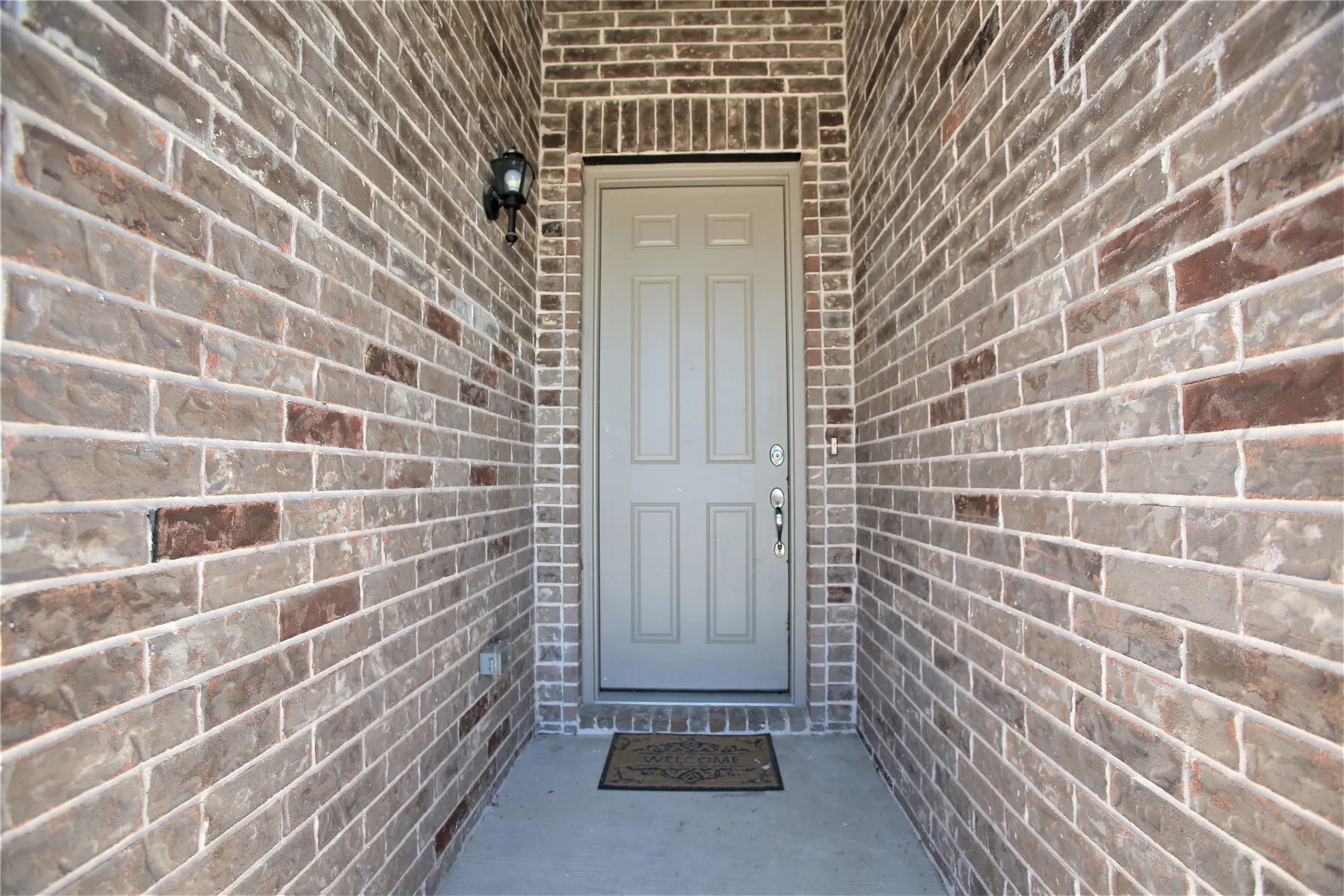 Entryway featuring variegated brick walls, a paneled door, black exterior sconce, and concrete flooring