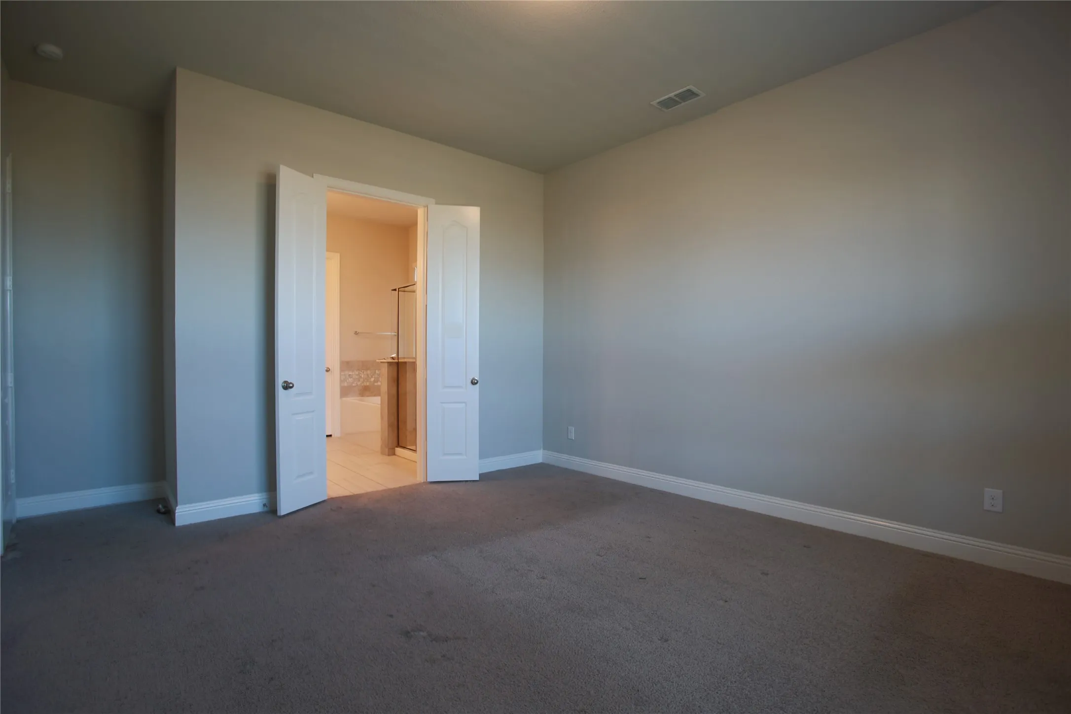 Carpeted bedroom featuring neutral paint, white trim, and double doors opening to a bathroom with tile flooring and a tiled bathtub surround