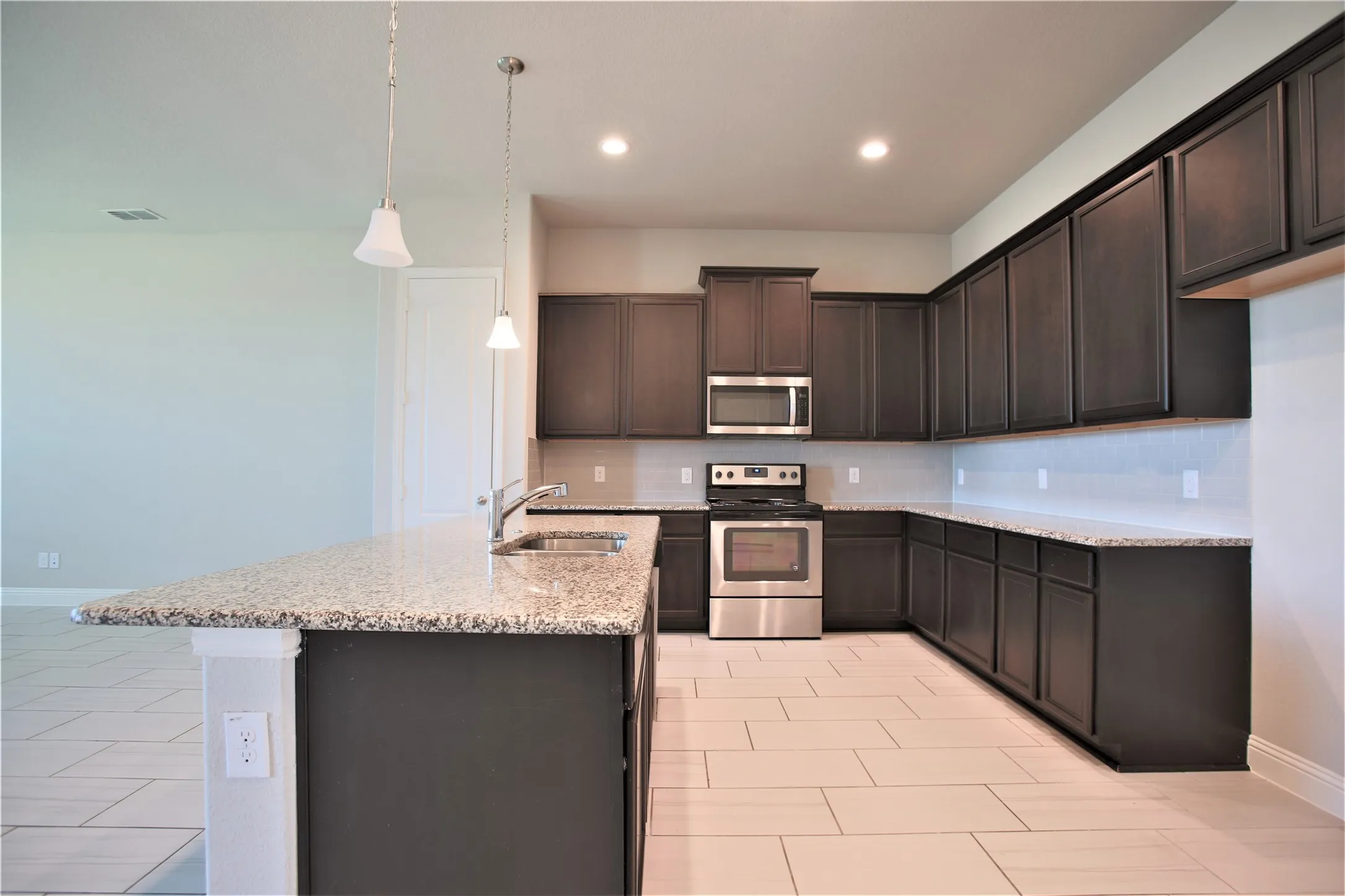 Modern kitchen featuring dark wood cabinetry, light-toned tile flooring, stainless steel appliances, granite countertops, and recessed lighting