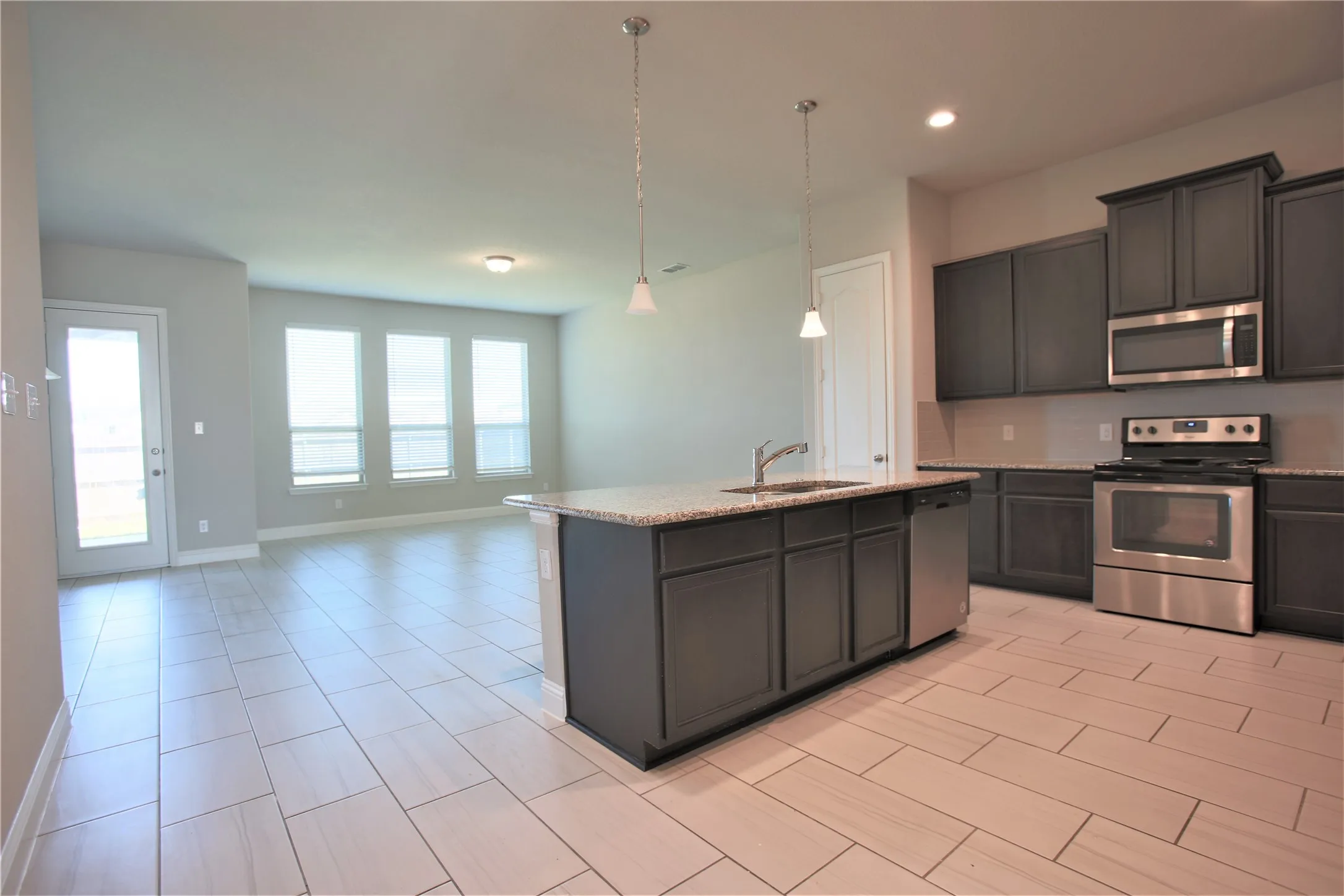 Open-concept kitchen featuring an island with a sink, pendant lighting, stainless steel appliances, and dark cabinetry