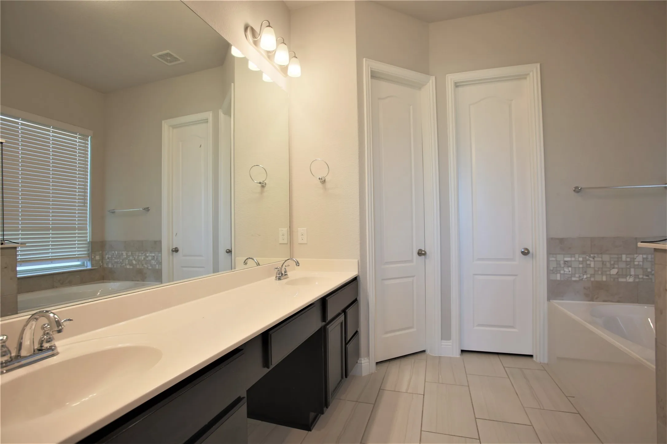 Dual sink vanity with dark cabinetry and light-colored countertops