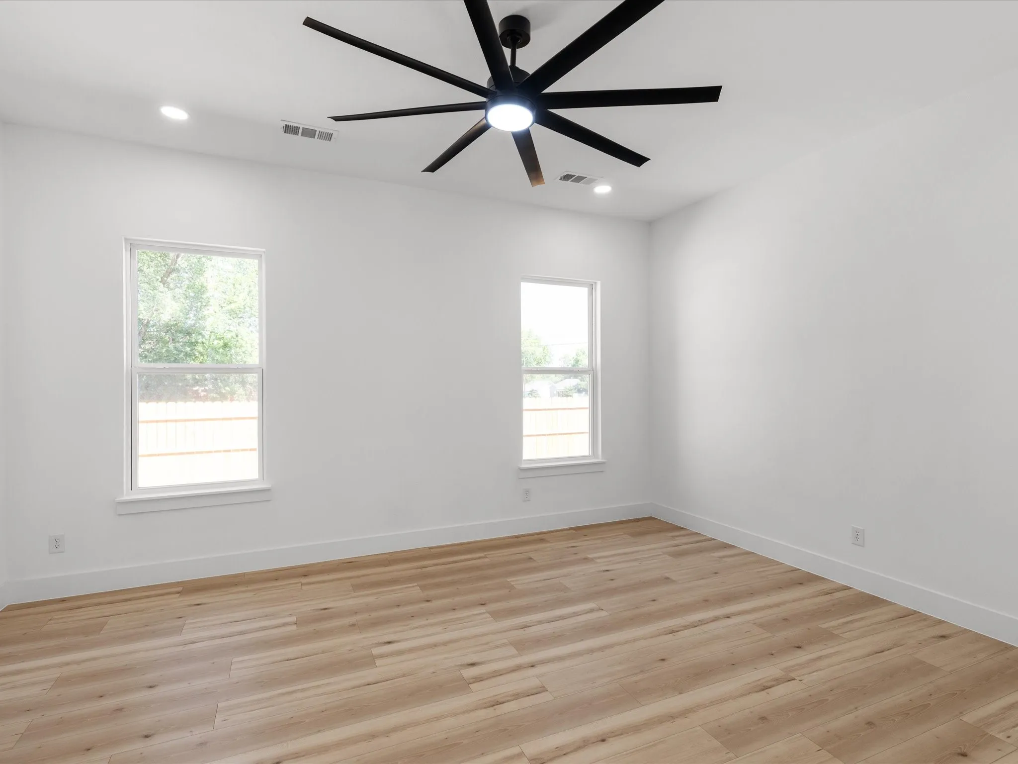Spacious room featuring wood-finish flooring, crisp white walls, and two large windows