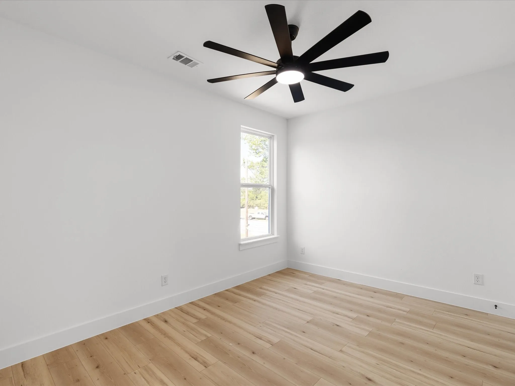 Bedroom featuring a modern black ceiling fan with integrated lighting, wood-finish flooring, white walls, and a white-framed window