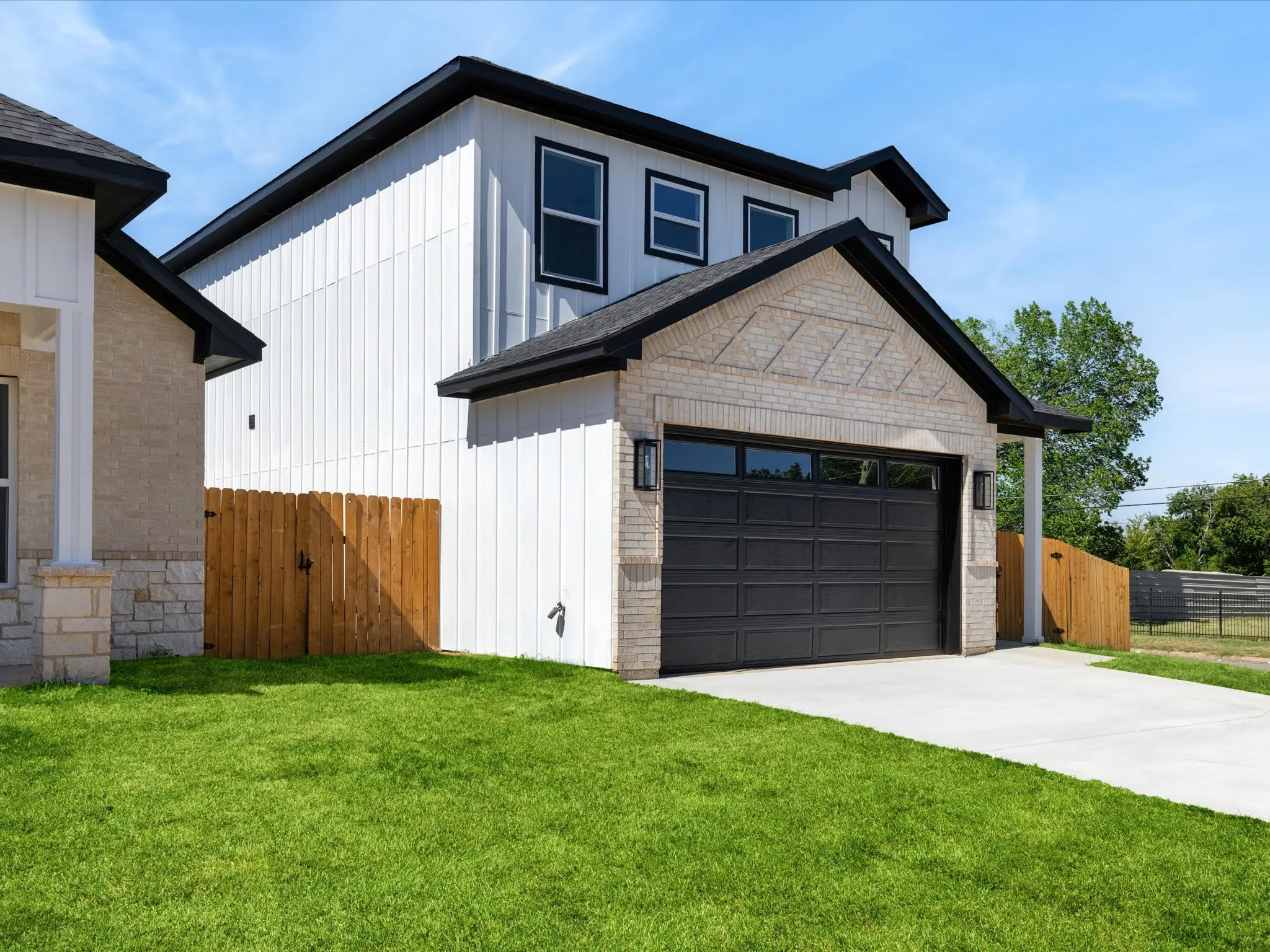 Modern exterior featuring a dark paneled garage door, light brickwork, white vertical siding, and a wooden privacy fence