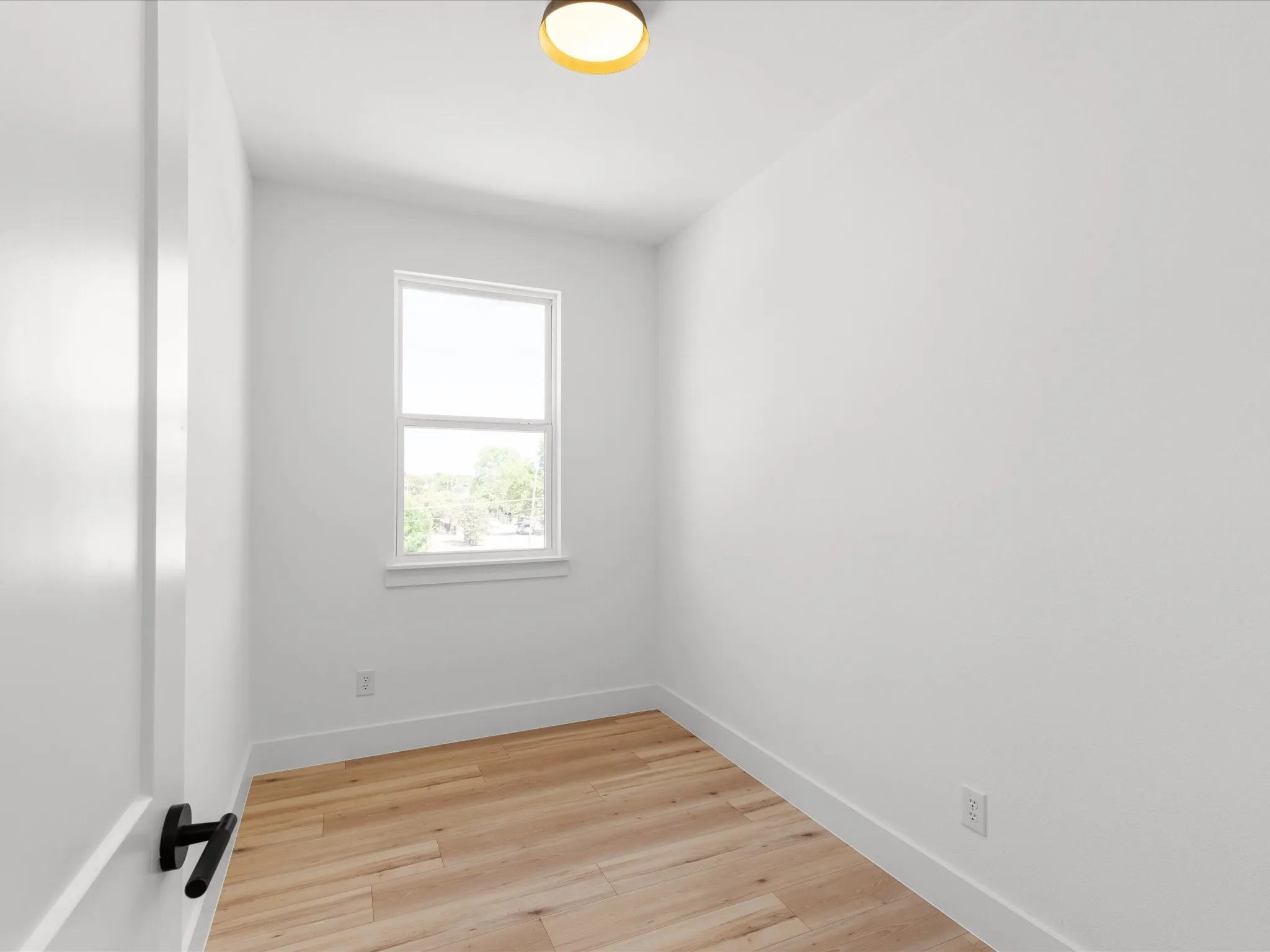 Compact room featuring light wood-finish flooring and a single window with white trim