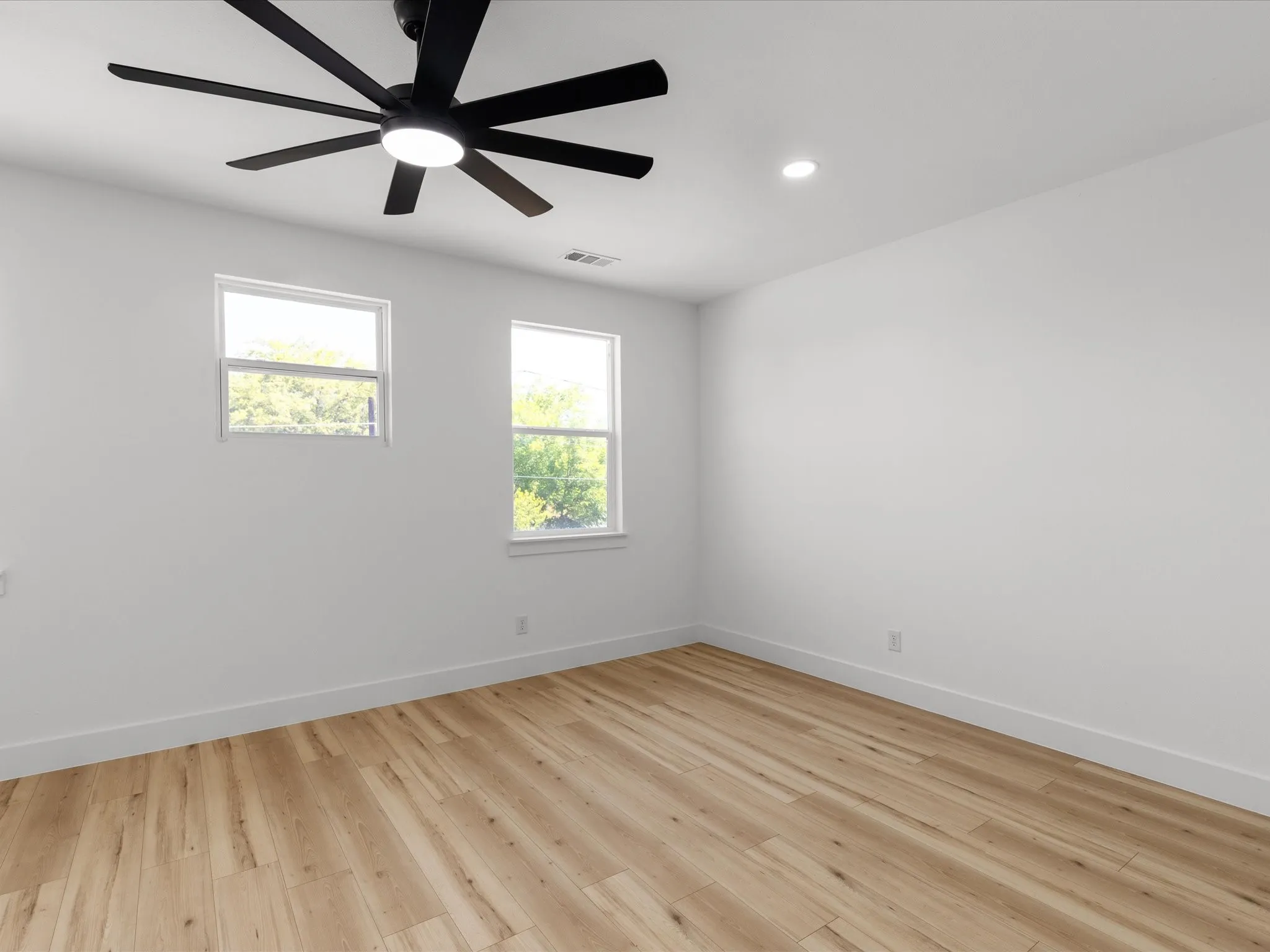 Room featuring a multi-blade ceiling fan with integrated lighting, recessed ceiling light, two windows, wood-finish flooring, and white baseboards