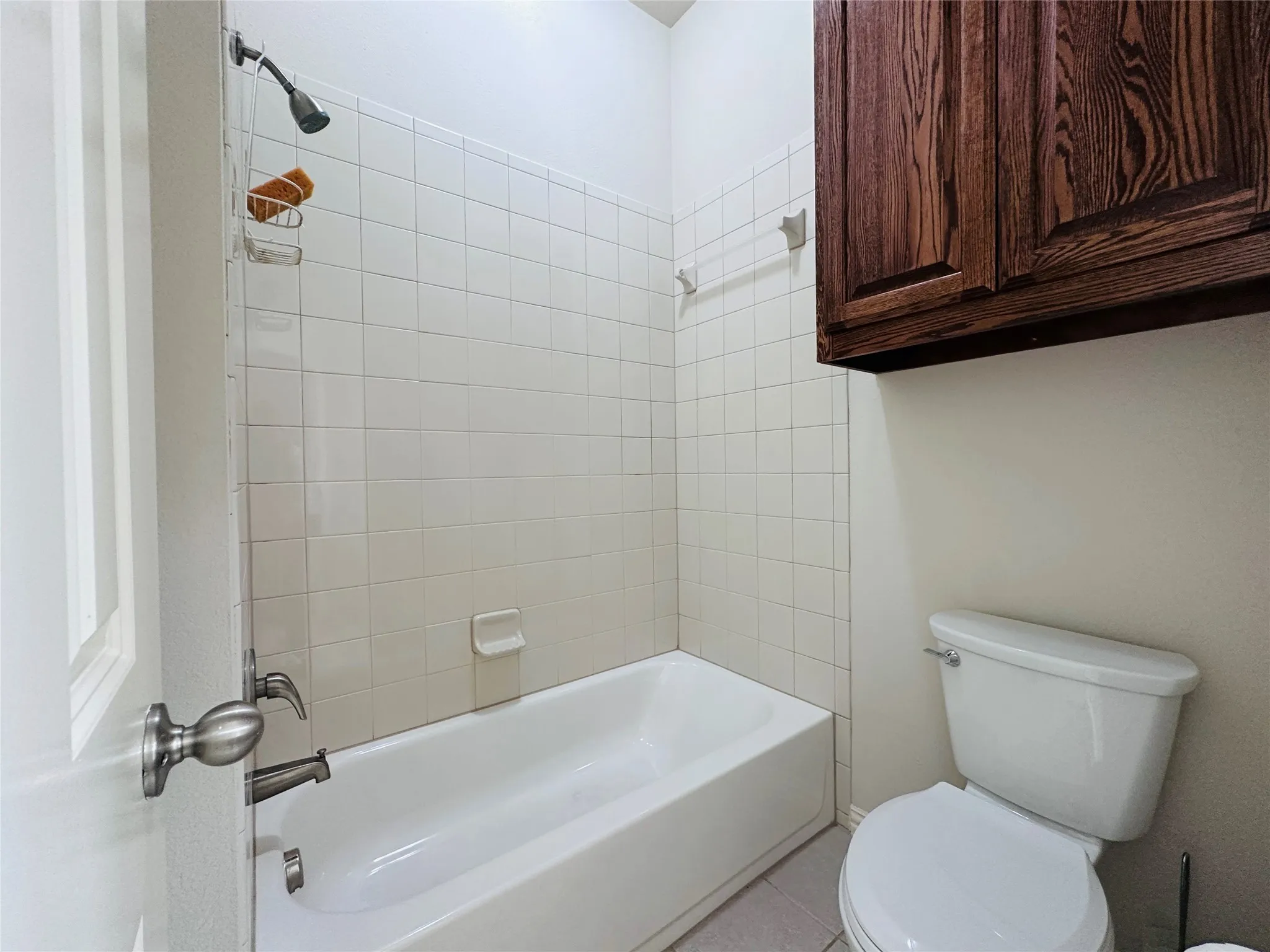 Bathroom featuring white subway tile surround, white bathtub, wood-finish cabinetry, and a white toilet