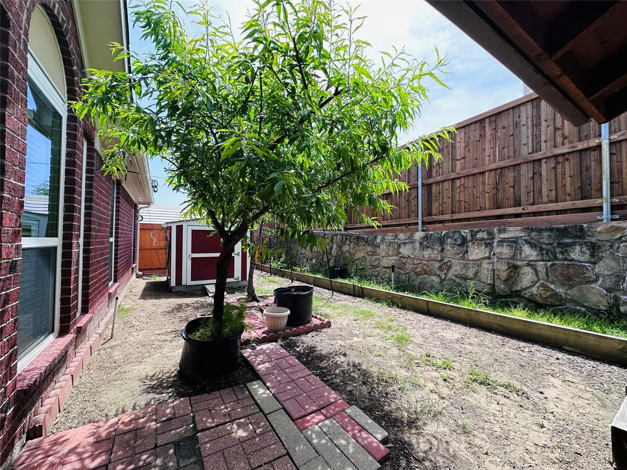 Side yard featuring a potted tree, brick paver accents, and a stone retaining wall