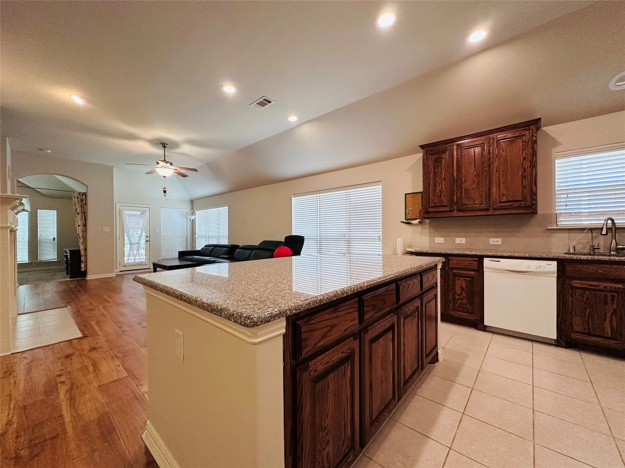 Kitchen island with a granite-style countertop, rich wood-finish cabinetry, and ceramic tile flooring