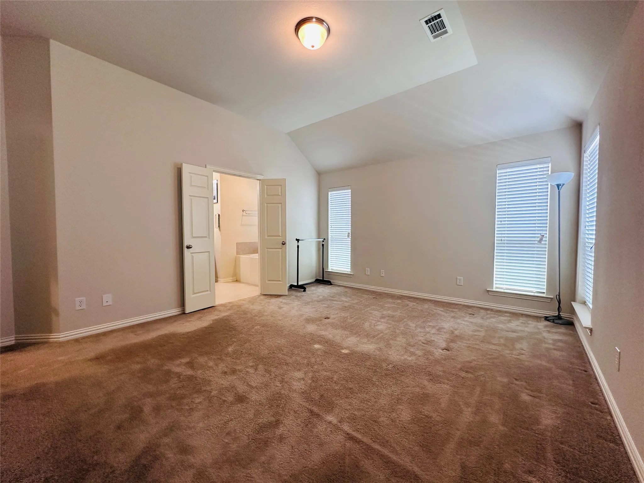 Spacious room featuring vaulted ceilings, a ceiling-mounted light fixture, and two tall windows with blinds