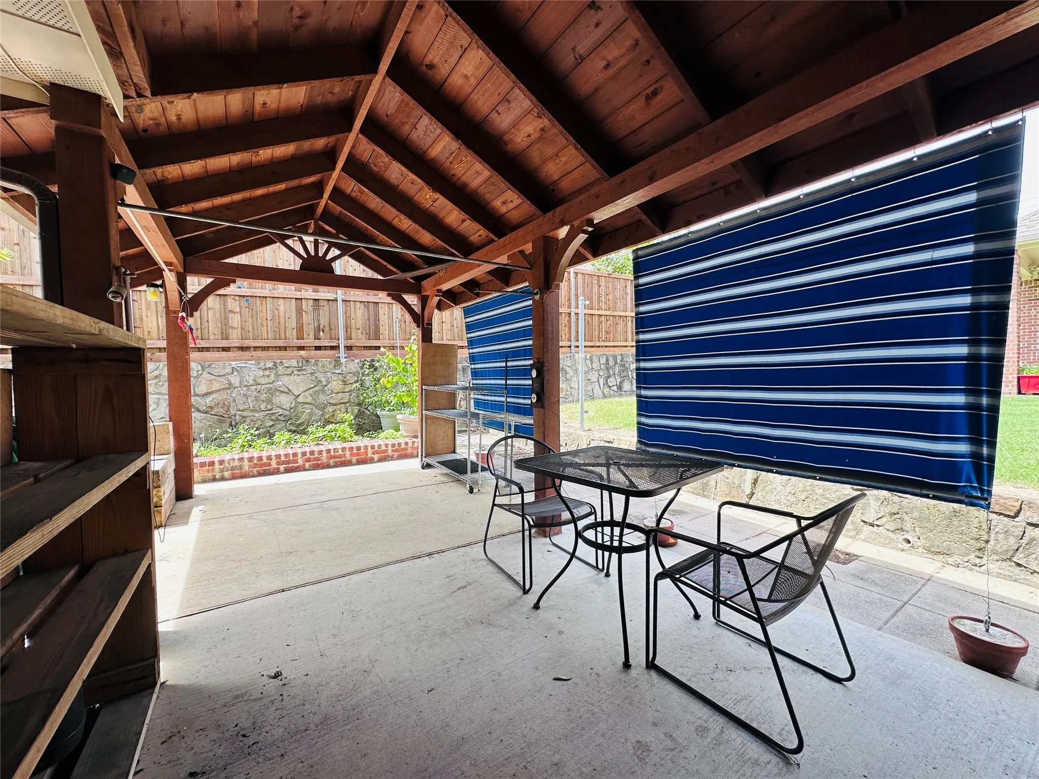 Covered patio featuring an exposed beam wood ceiling, concrete flooring, and privacy screens
