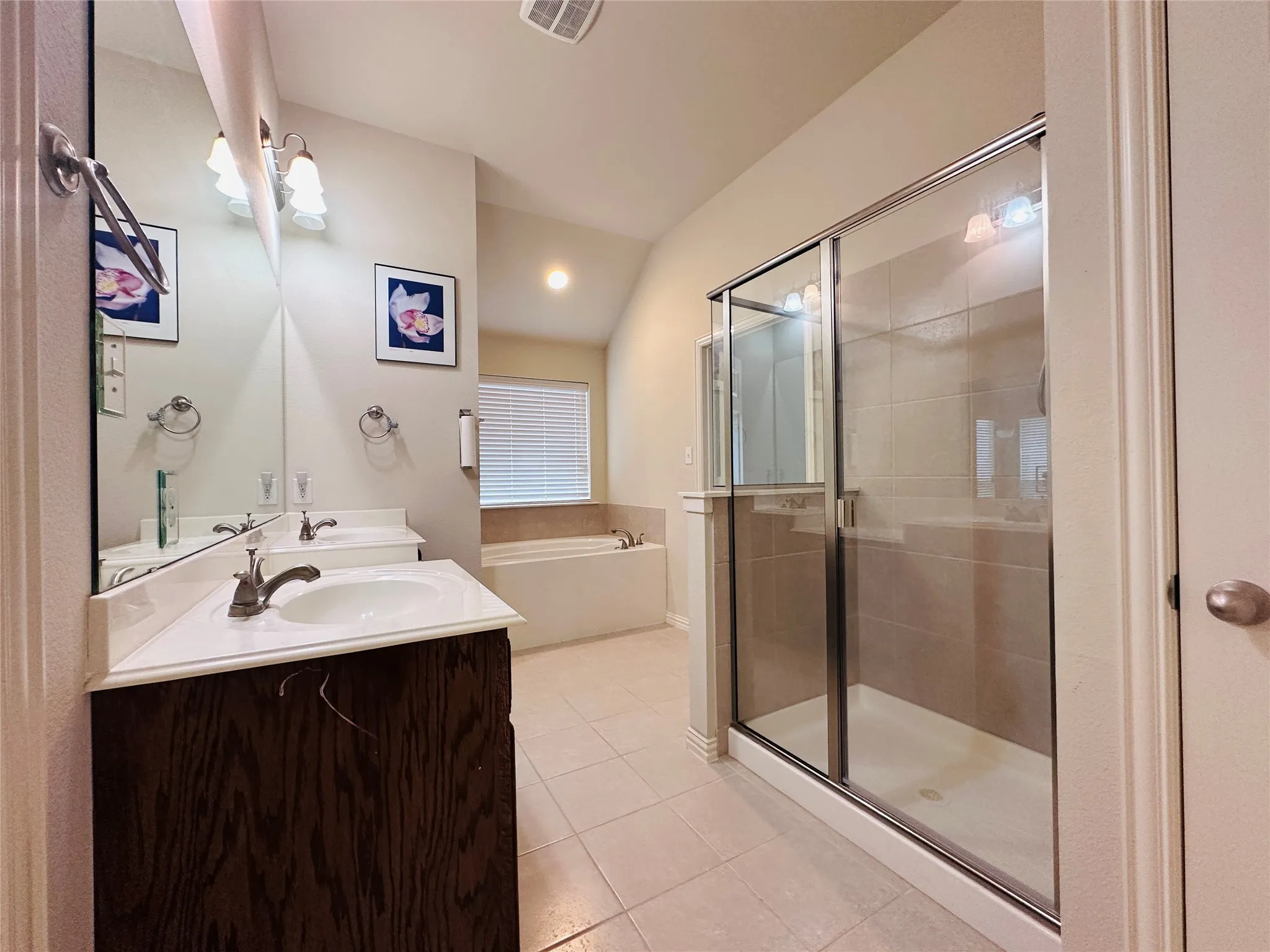 Bathroom featuring a glass-enclosed shower, dual vanities with integrated sinks, a built-in soaking tub, tile flooring, and a window with blinds