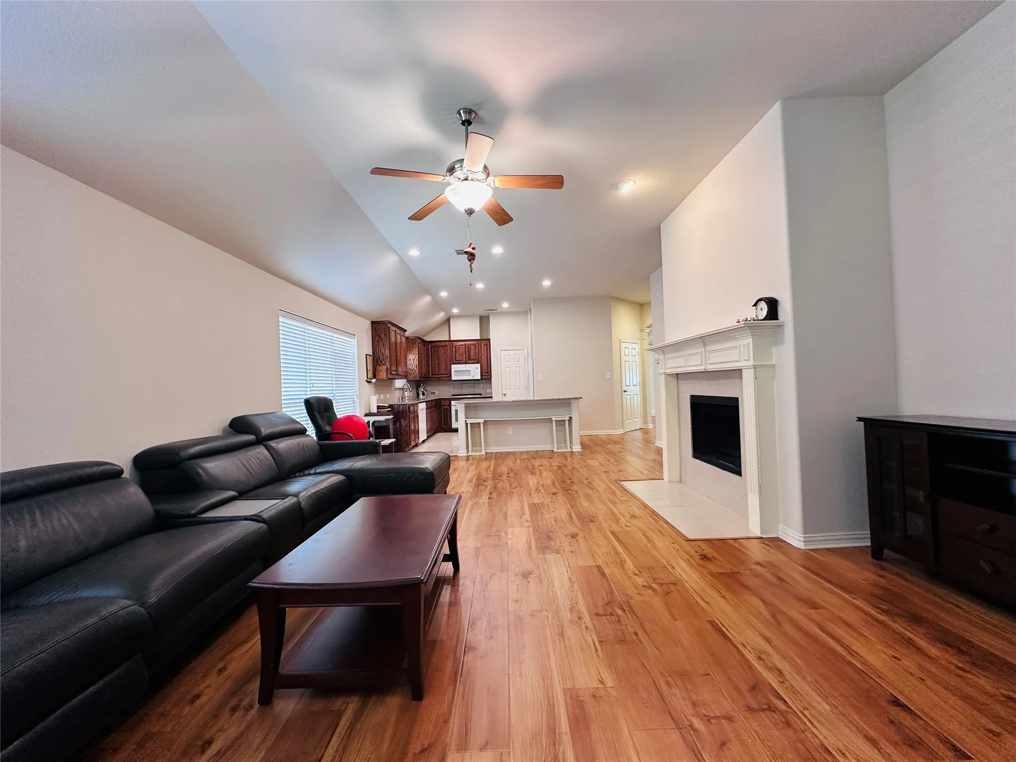 Open-concept living space featuring wood-finish flooring, a white mantel fireplace, and a ceiling fan