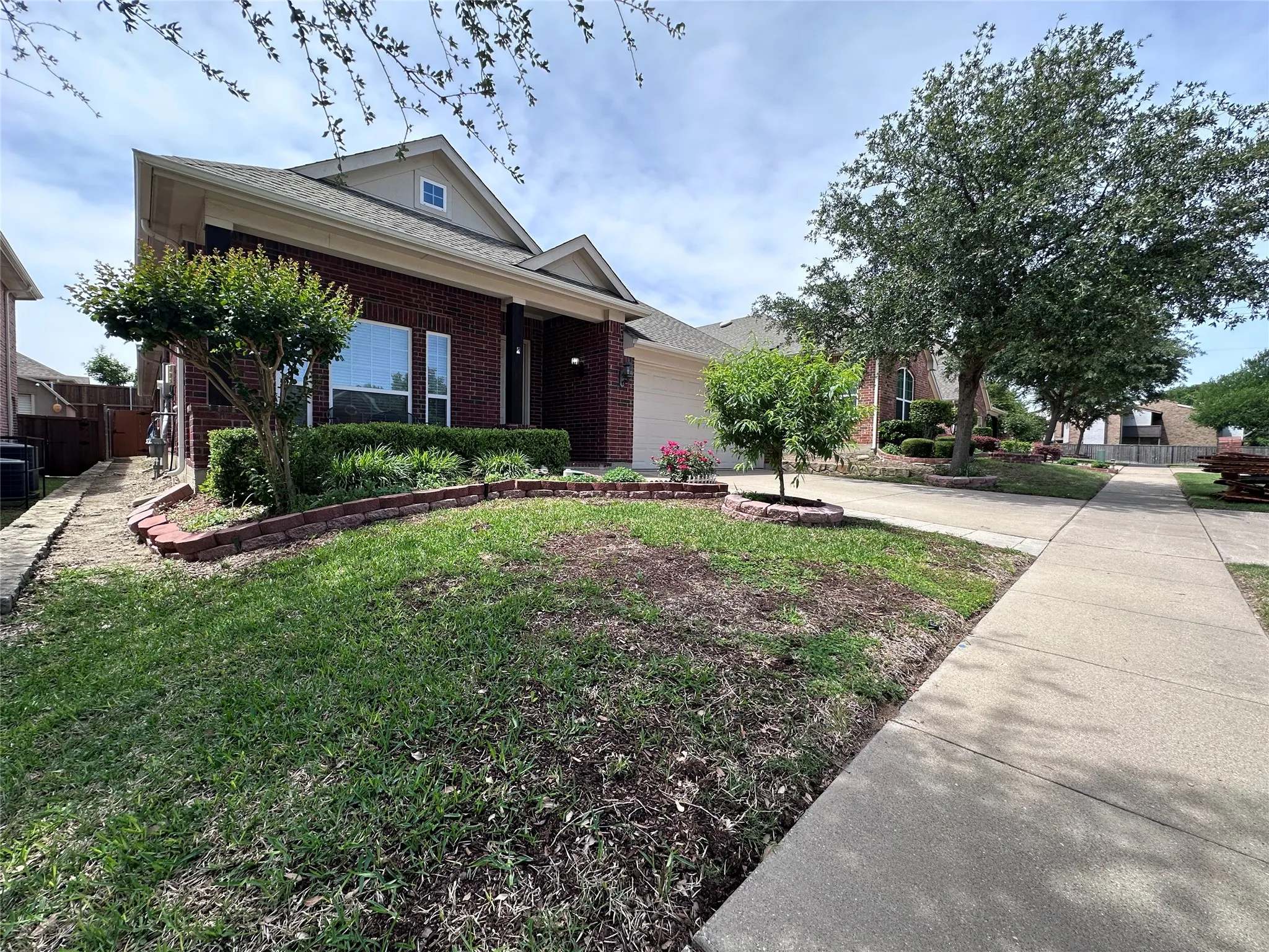 Traditional brick exterior with an attached garage, pitched roof, and a front yard featuring a landscaped bed with red brick edging