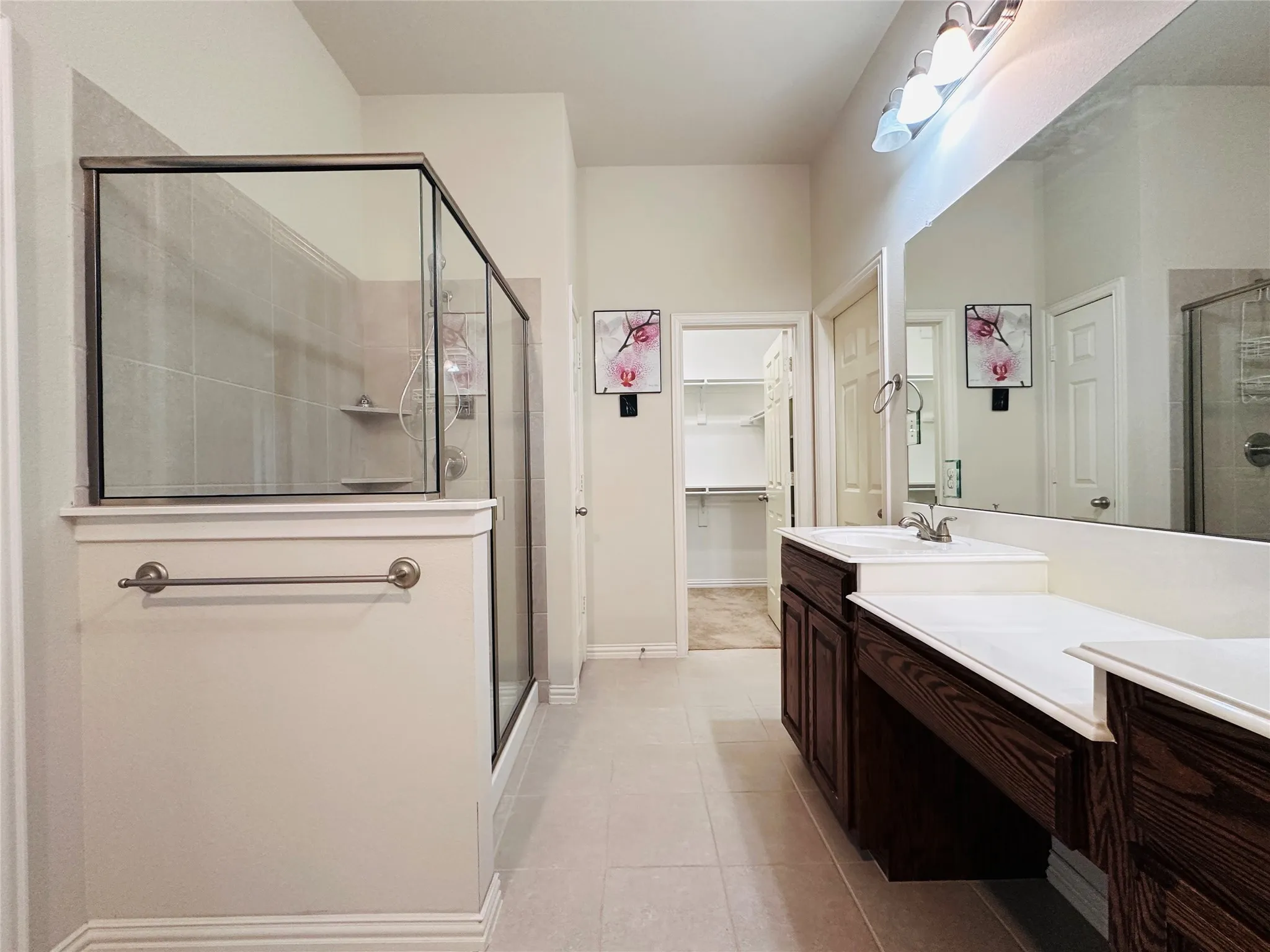 Bathroom featuring a glass-enclosed shower, dual vanities with integrated sinks, dark wood-finish cabinetry, and a full-width mirror