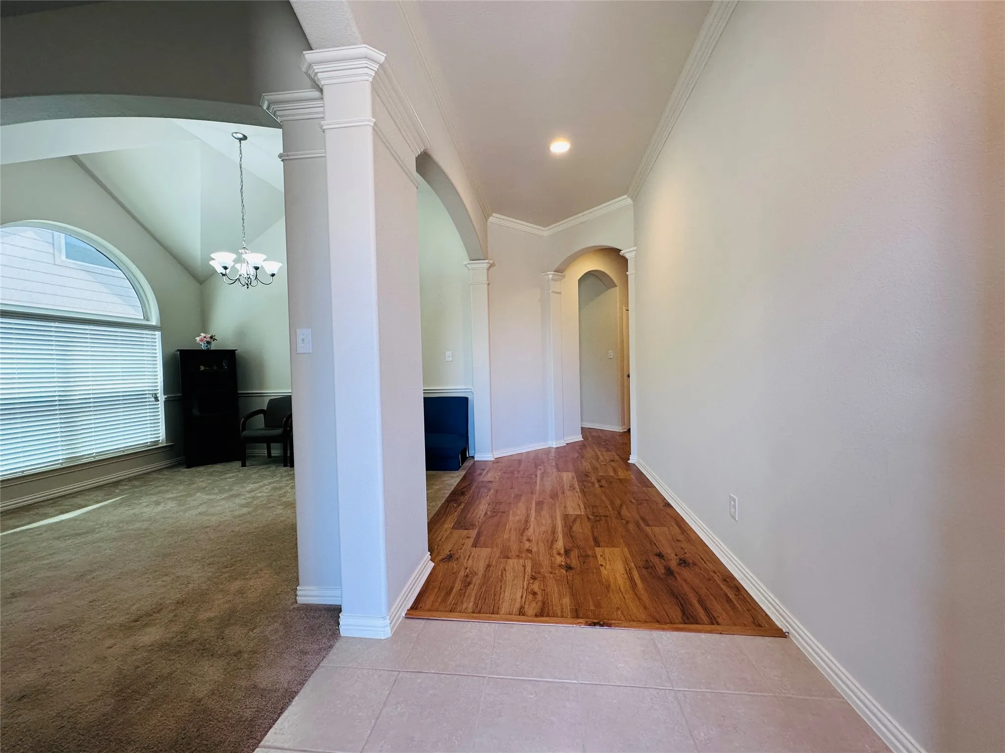 Foyer featuring tile flooring transitioning to wood-finish flooring, arched doorways, crown molding, and a recessed ceiling light