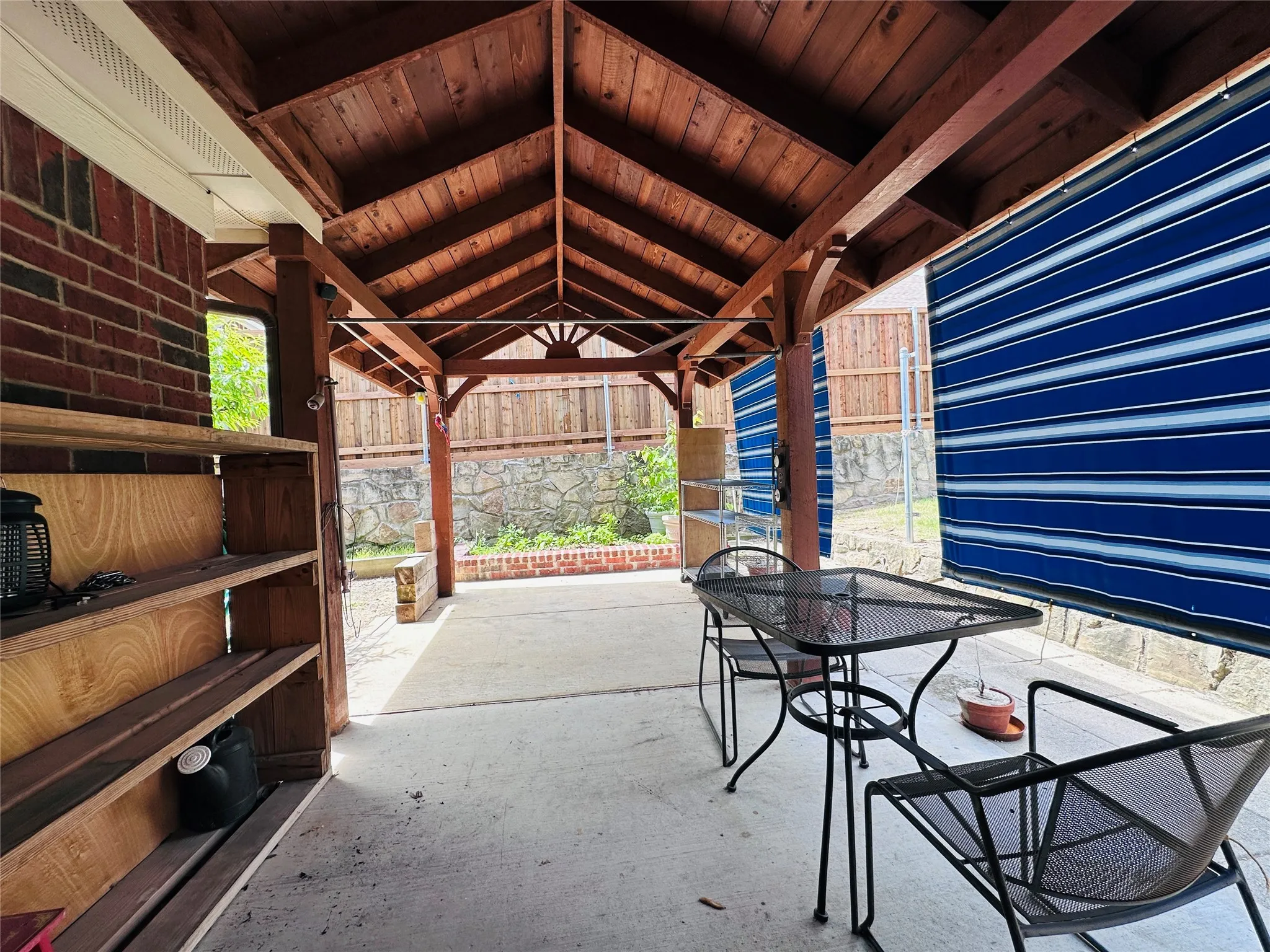 Covered patio featuring a wood-beam ceiling, concrete flooring, and an exposed brick wall