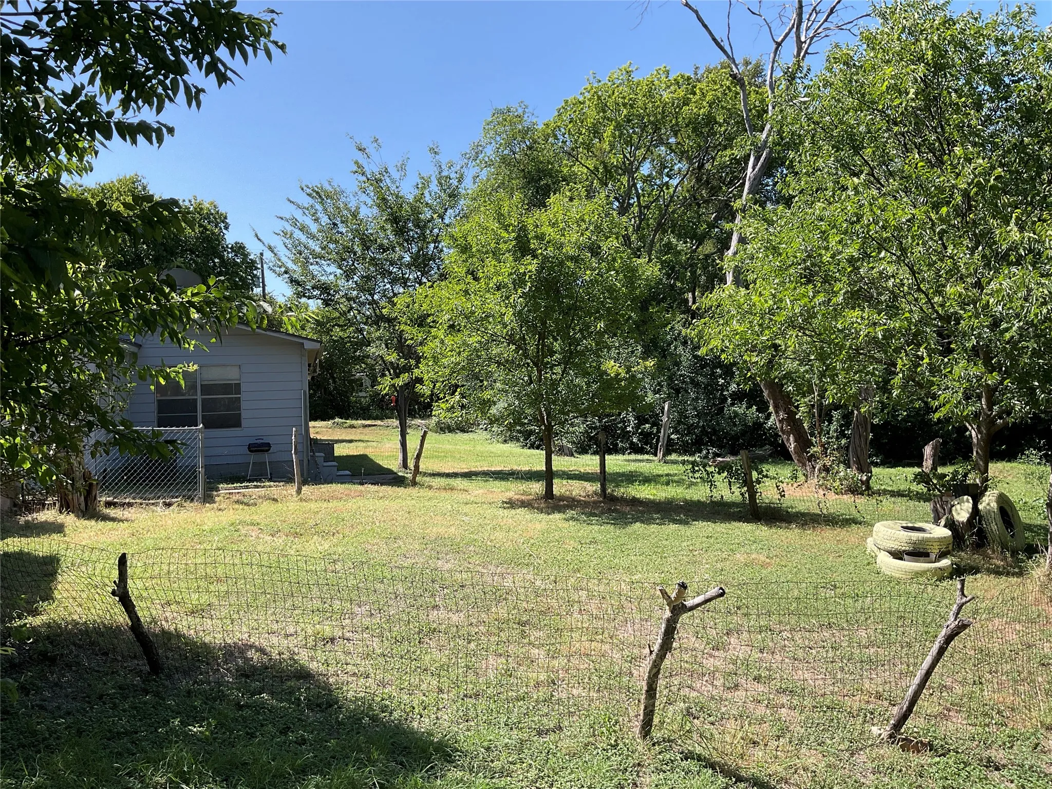 Expansive backyard featuring a partial chain-link fence, mature trees, and a grassy lawn