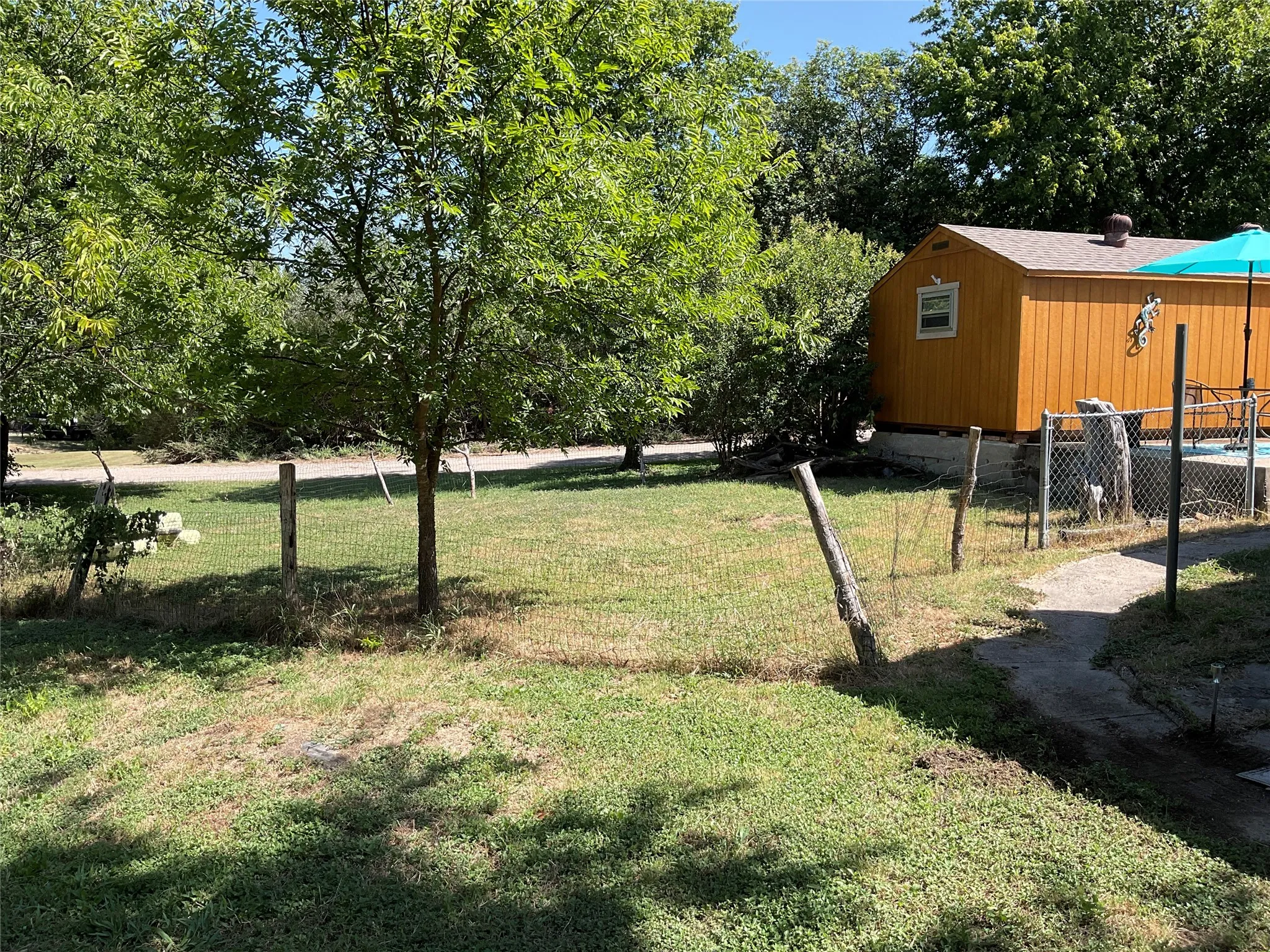 Expansive grassy area featuring mature trees with garden area or dog run