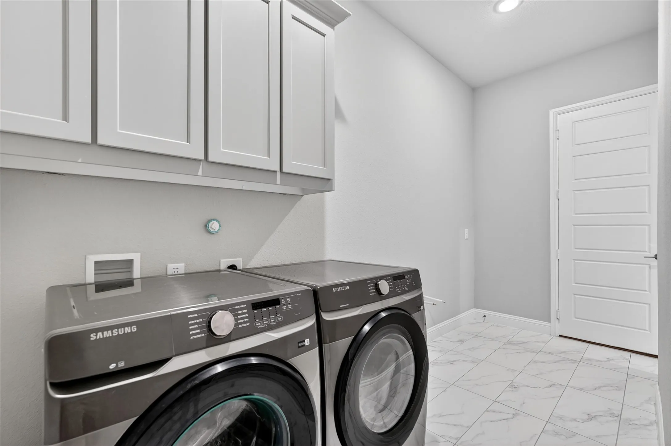 Utility room featuring overhead shaker-style cabinetry, a white paneled door, light gray walls, recessed lighting, and white tile flooring