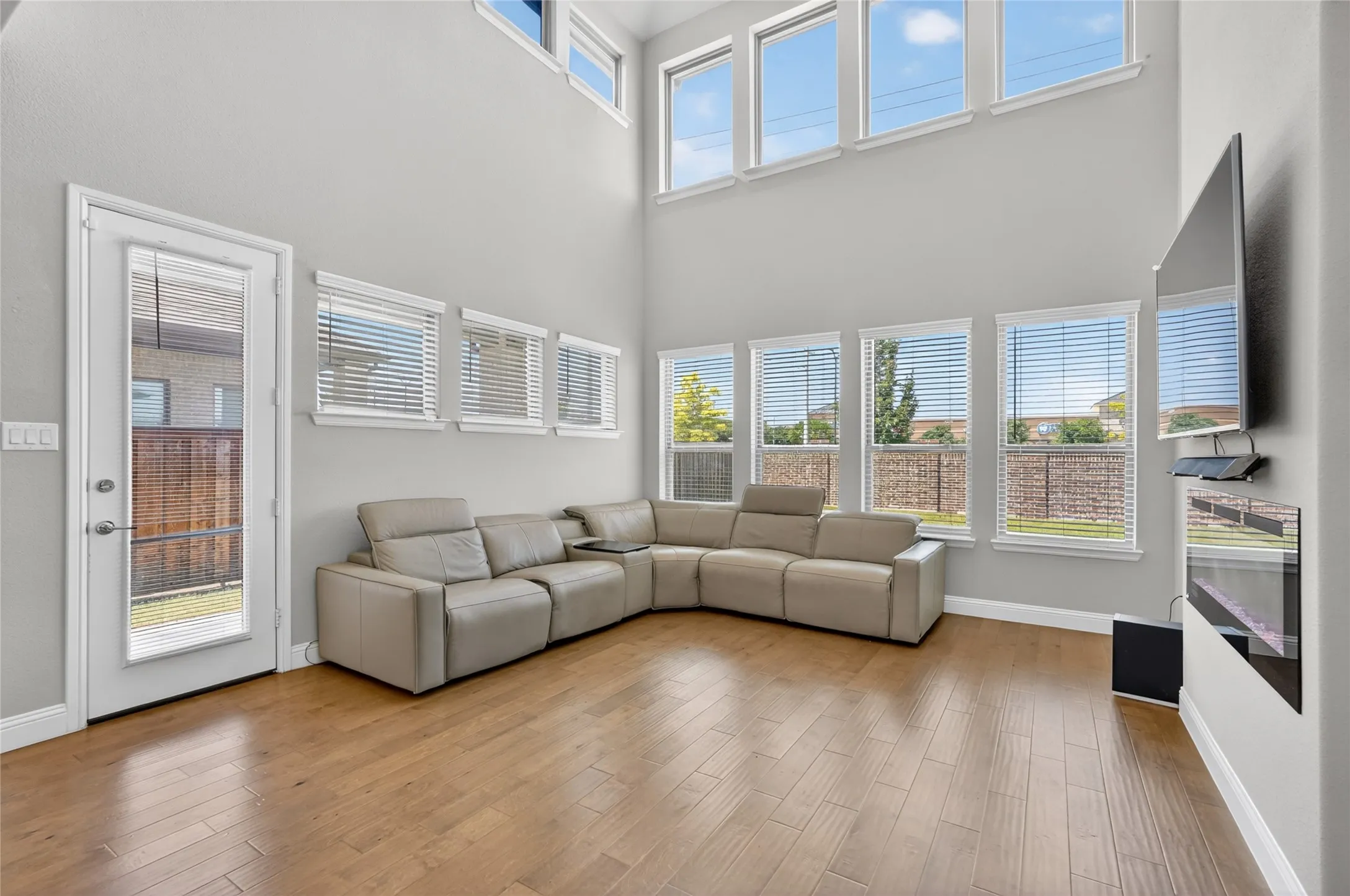 Living area featuring wood-finish flooring, a full-lite glass panel door, and multiple windows with horizontal blinds