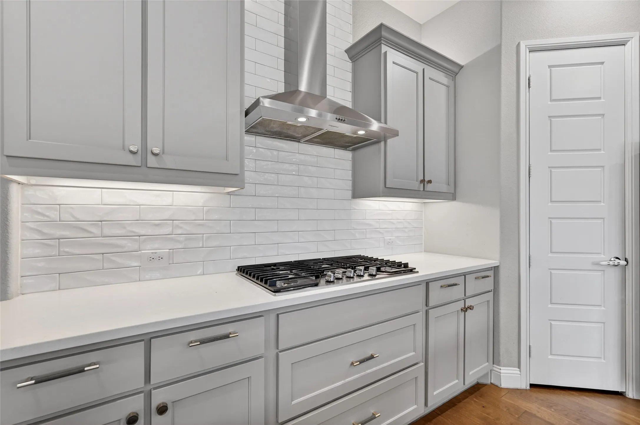 Modern kitchen featuring light gray cabinetry with brushed nickel hardware, white stone-finish countertops, and a textured subway tile backsplash