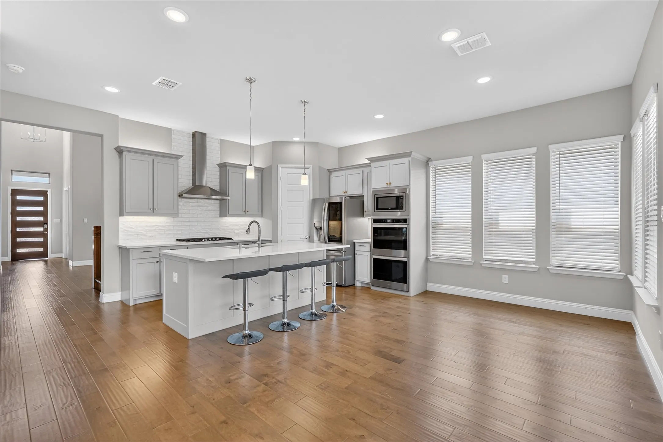 Open-concept kitchen and living area featuring wood-finish flooring, recessed lighting, and multiple windows with blinds