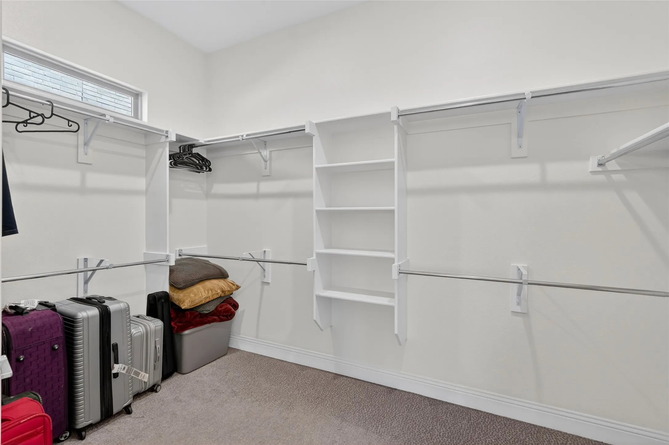 Spacious walk-in closet featuring built-in shelving, multiple hanging rods, and a high window
