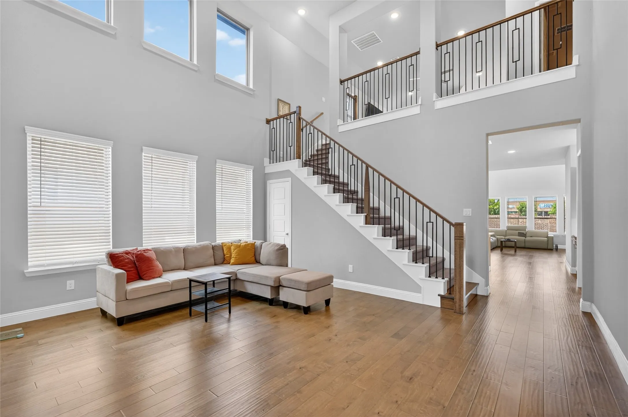 Two-story living area with high ceilings, wood-finish flooring, and multiple windows